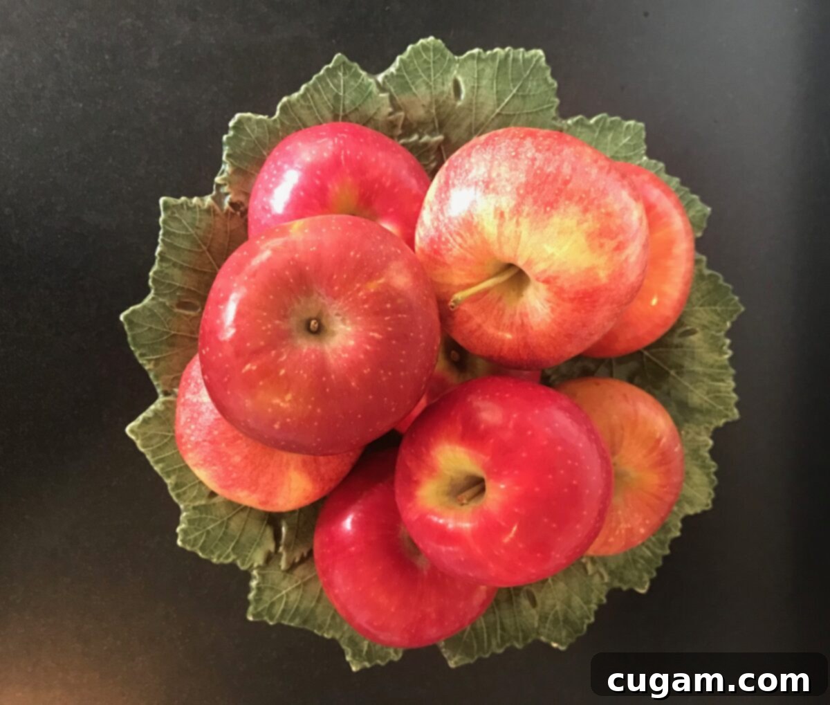 Green leafy ceramic pedestal dish with an assortment of fresh apples on top.
