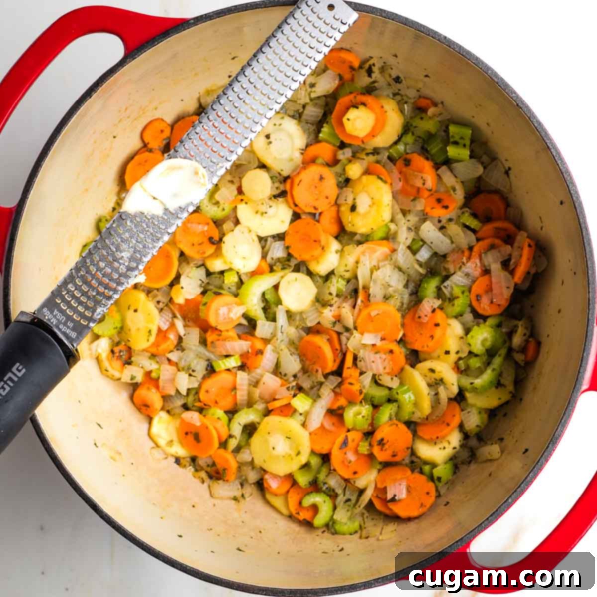 Grating garlic over a dutch oven with sauteed veggies.