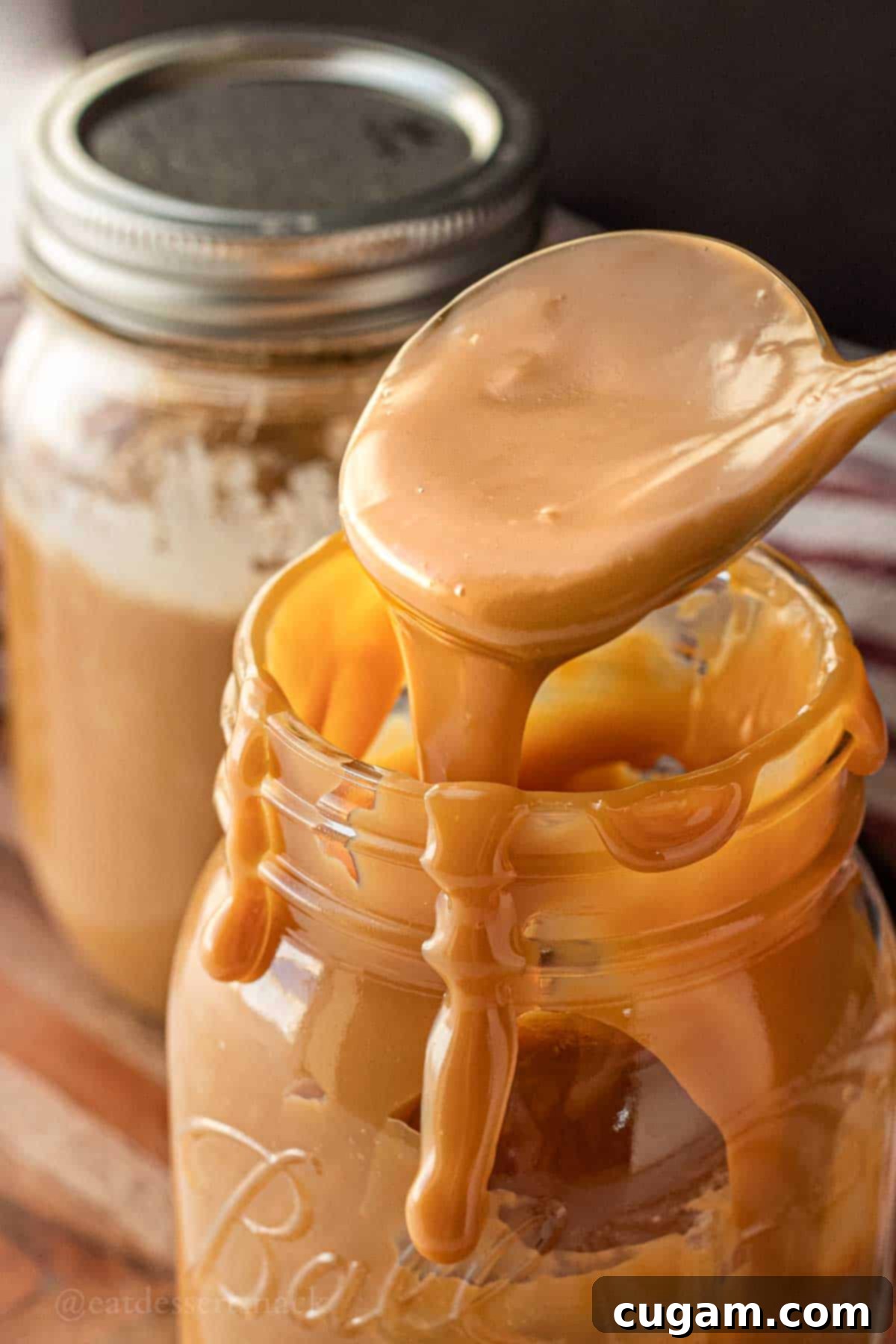 Easy Instant Pot Dulce De Leche 2 A spoon drizzling rich, homemade Instant Pot Dulce de Leche over a glass jar, showcasing its smooth, creamy texture.