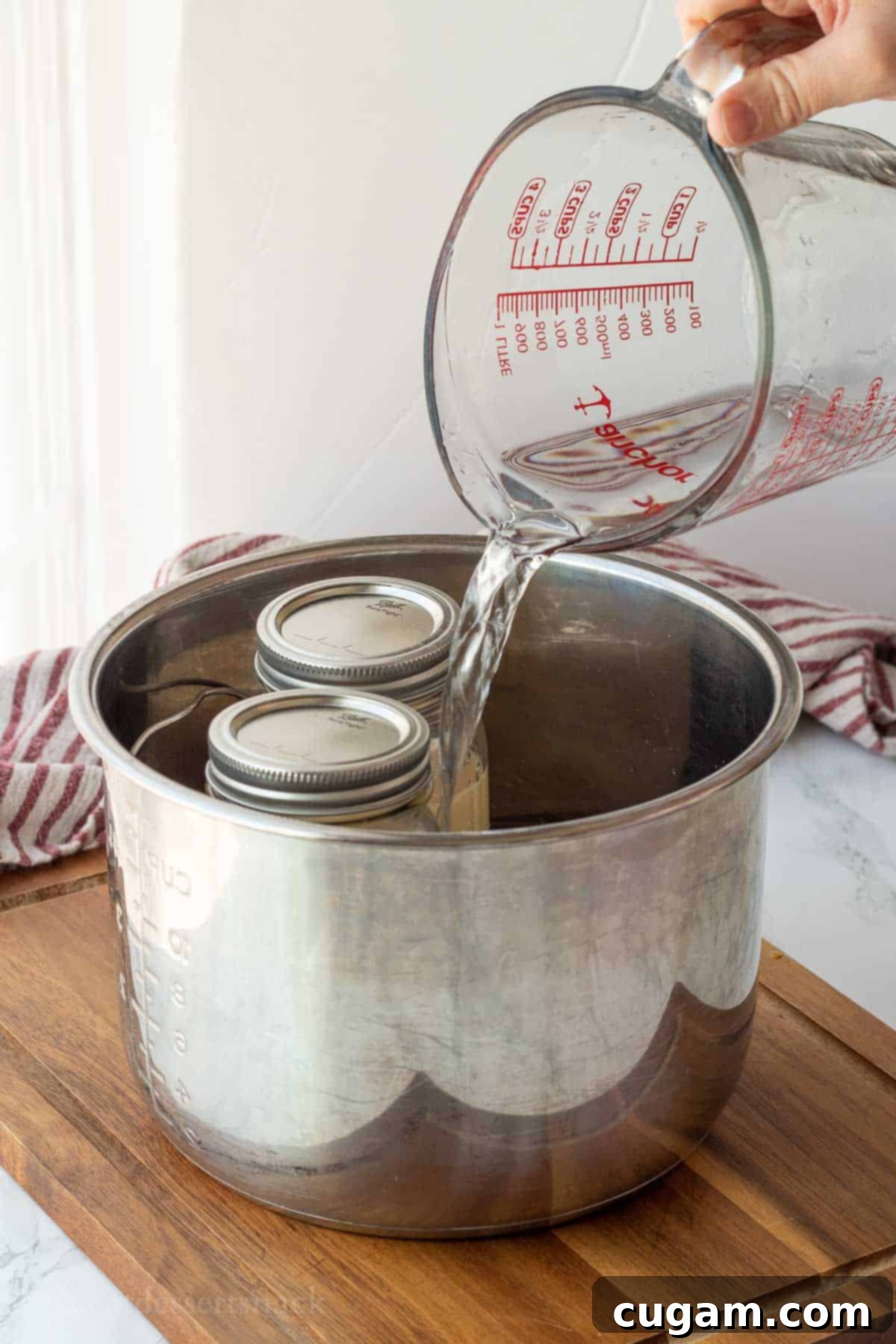 Easy Instant Pot Dulce De Leche 5 A glass measuring cup pouring water into the Instant Pot base with mason jars on a rack, illustrating the correct water level for cooking.