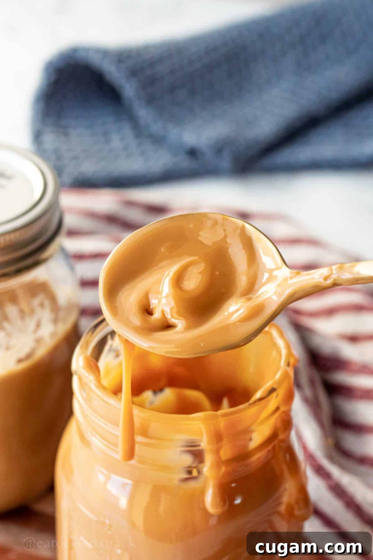 Easy Instant Pot Dulce De Leche 7 A spoonful of warm, glistening dulce de leche held above a glass jar, highlighting its smooth and rich texture.