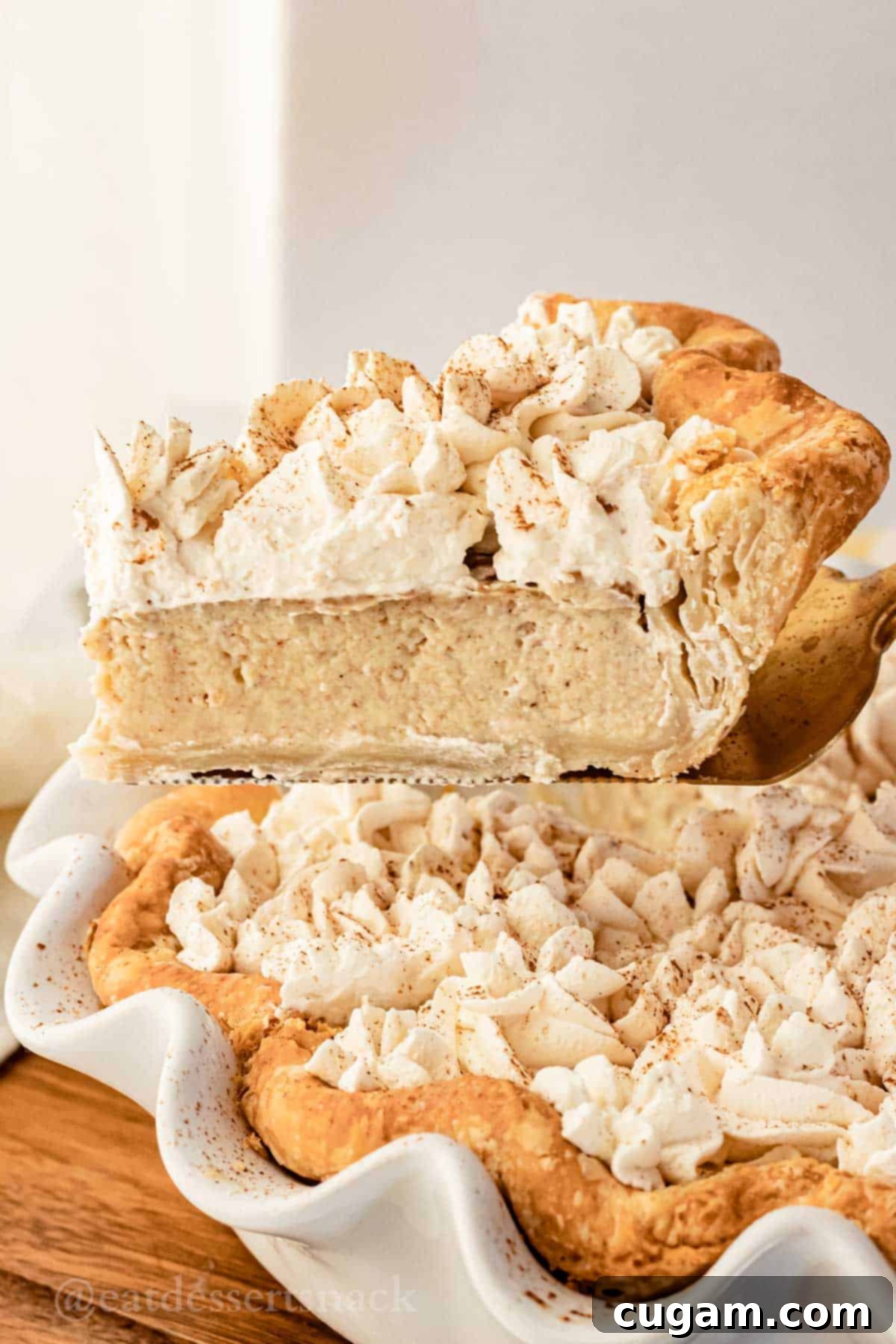 Single slice of baked banana cream pie on spatula above pie.
