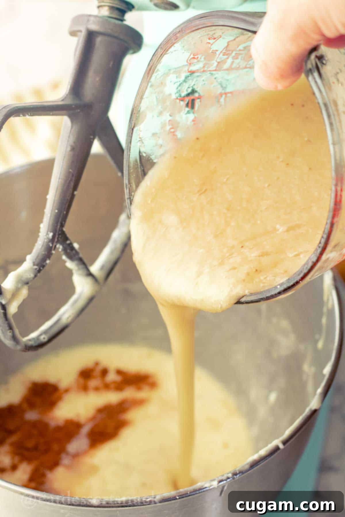 Glass measuring cup pouring banana puree into metal mixing bowl.