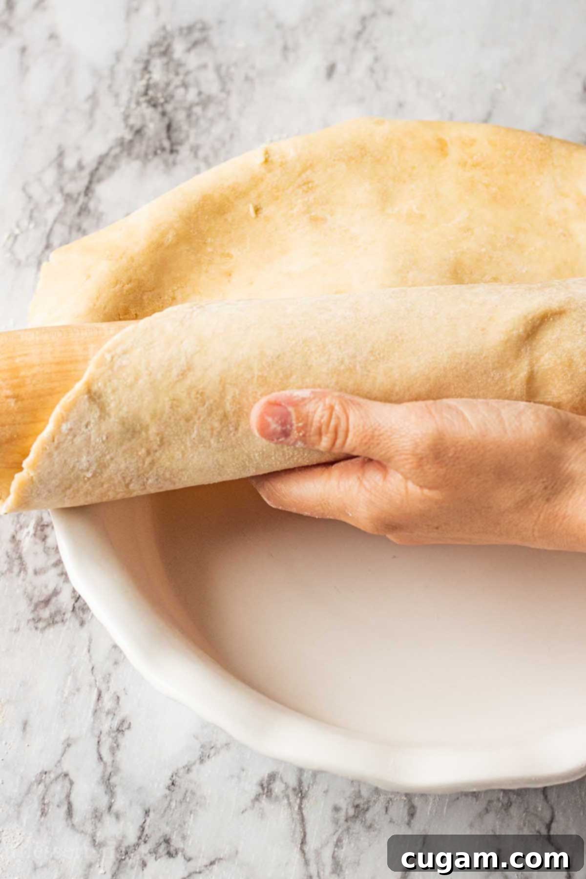Hand rolling pie crust into white pie dish.