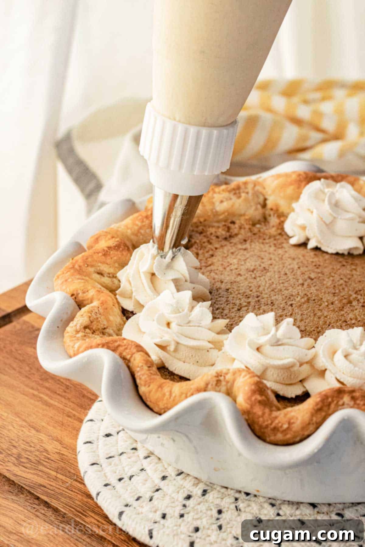 Frosting bag piping whipped cream onto cooled baked banana cream pie.