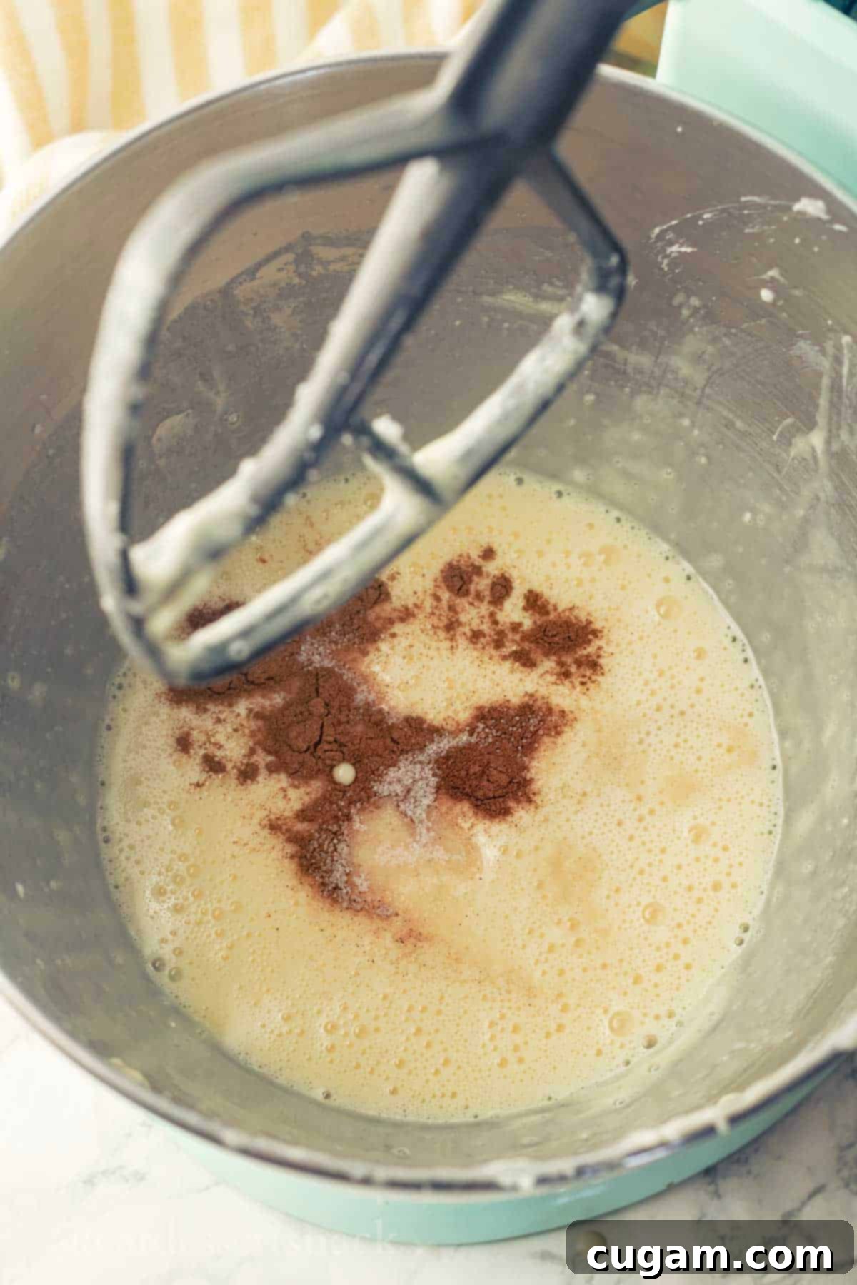 Cinnamon and eggs in metal mixing bowl with metal electric mixer paddle.