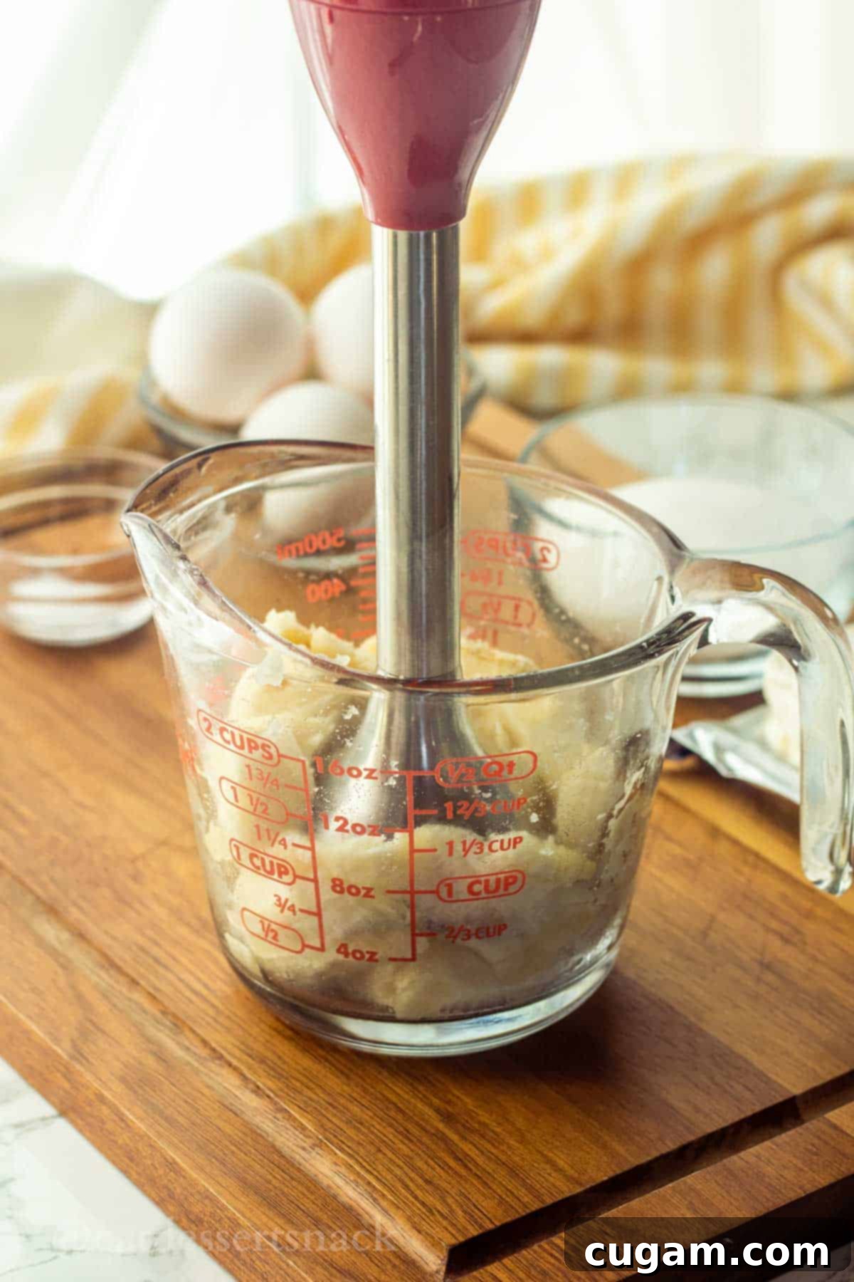 Immersion blender/masher in glass measuring cup blending the bananas.
