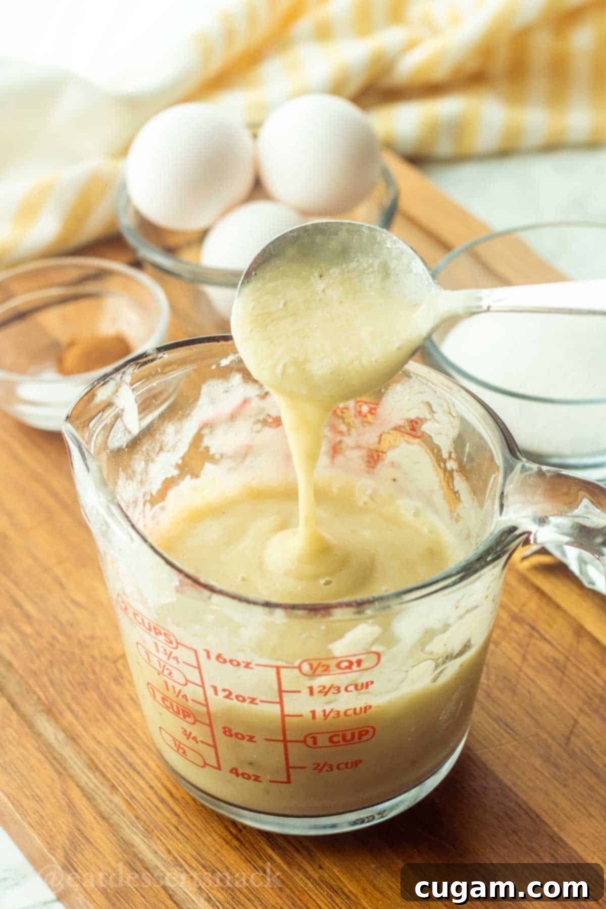 Spoonful of banana puree pouring into glass measuring cup.