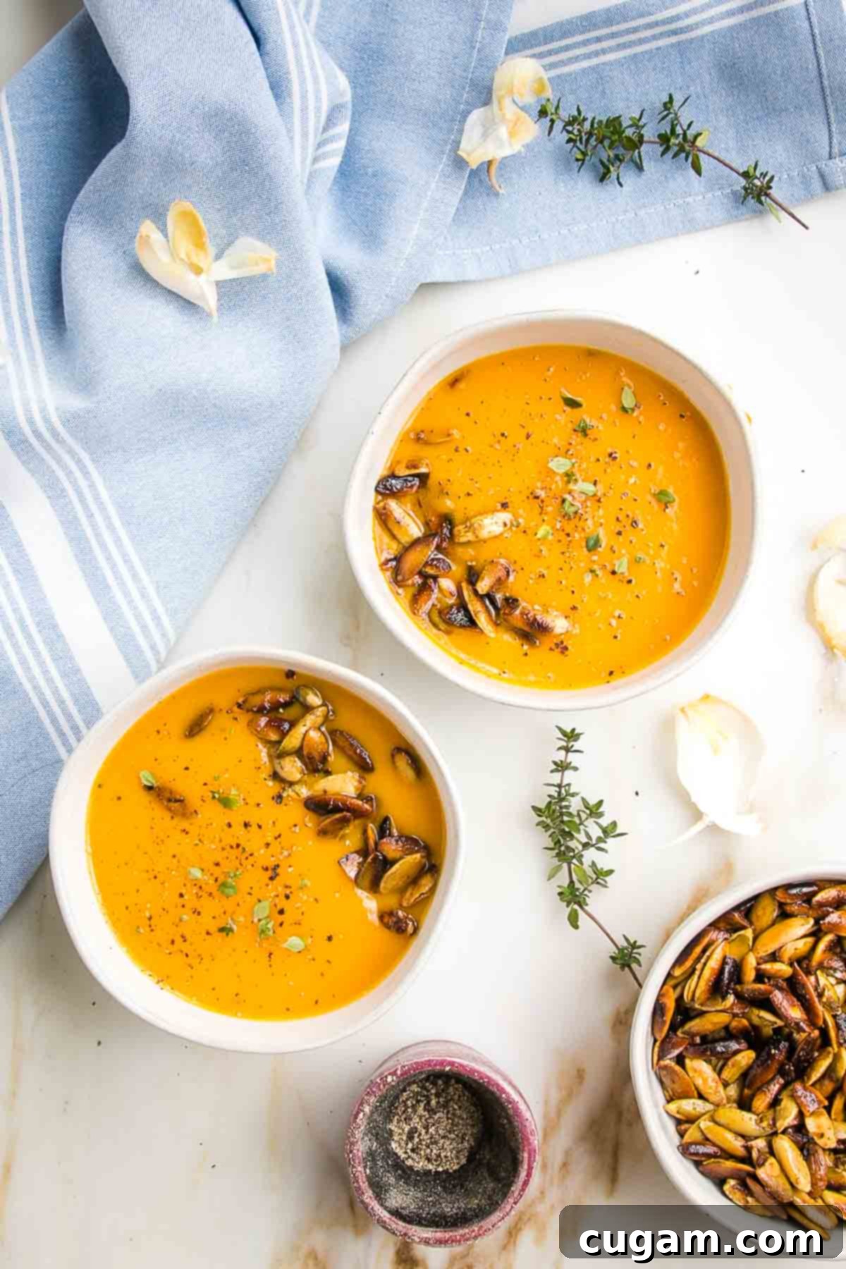 Two bowls of orange creamy soup, topped with toasted pumpkin seeds and a swirl of vegan sour cream. 