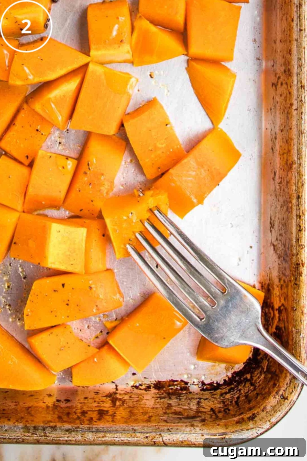 A fork piercing a cube of roasted squash on a large rimmed baking sheet.