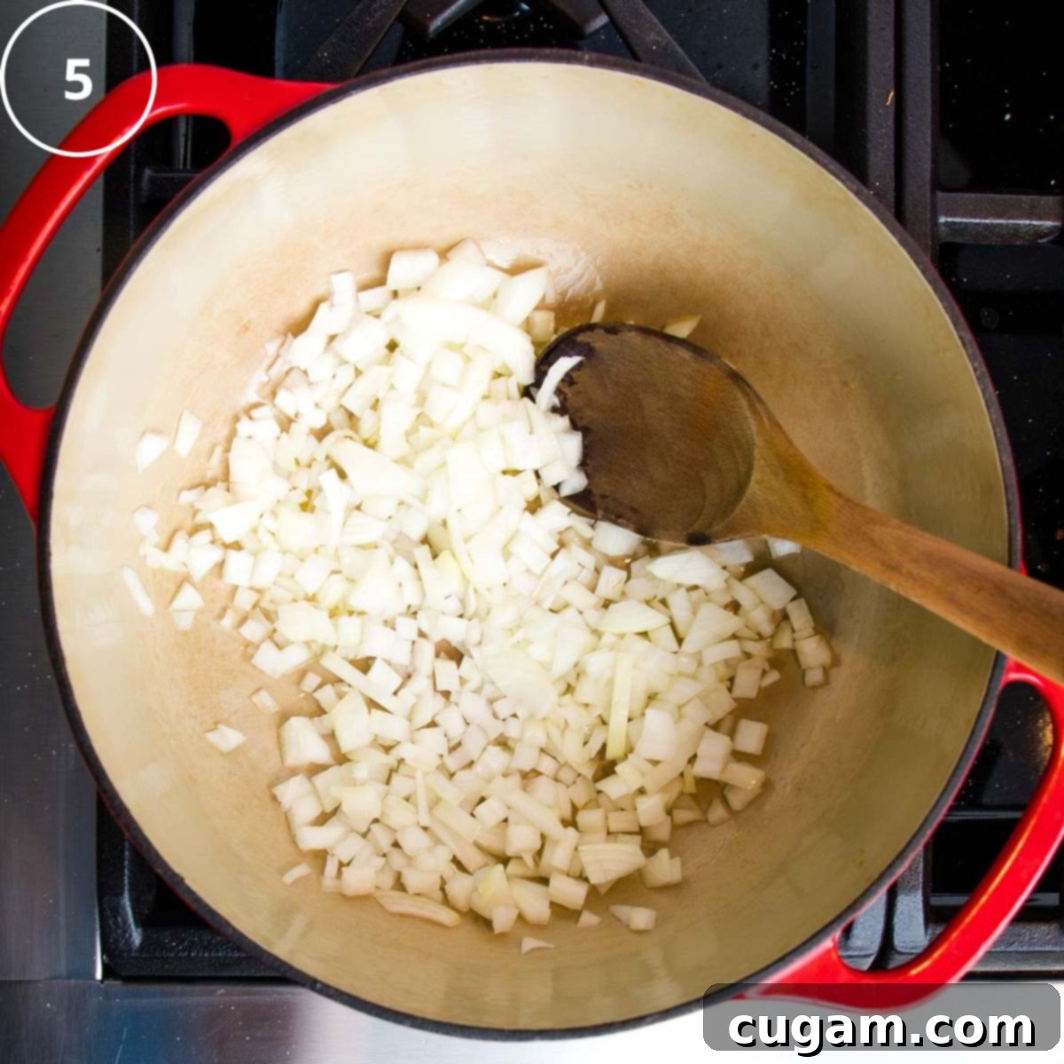 Diced onions in a dutch oven with a wooden spoon.