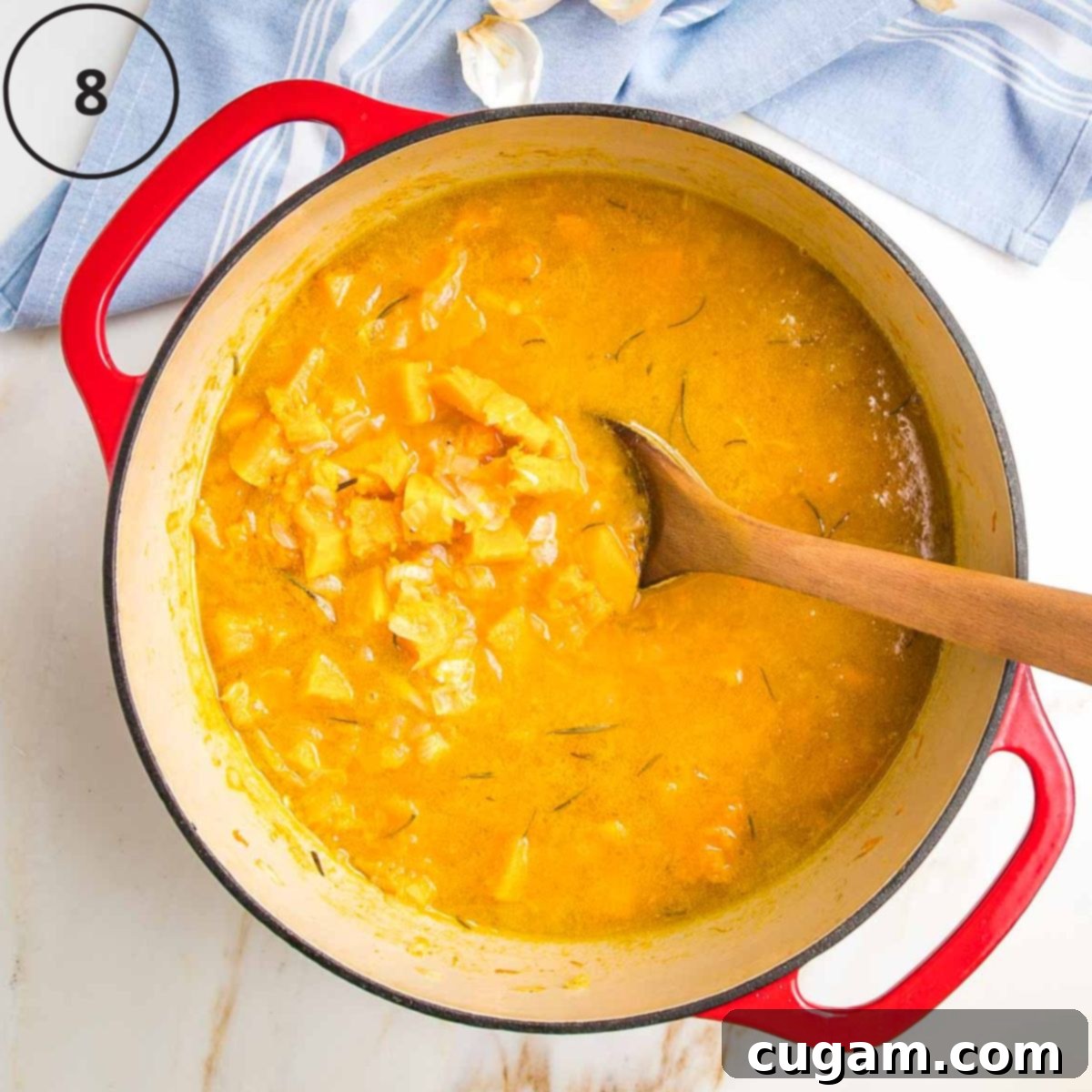 Butternut squash soup in a dutch oven, chunks of squash and onions floating in orange broth in a dutch oven.