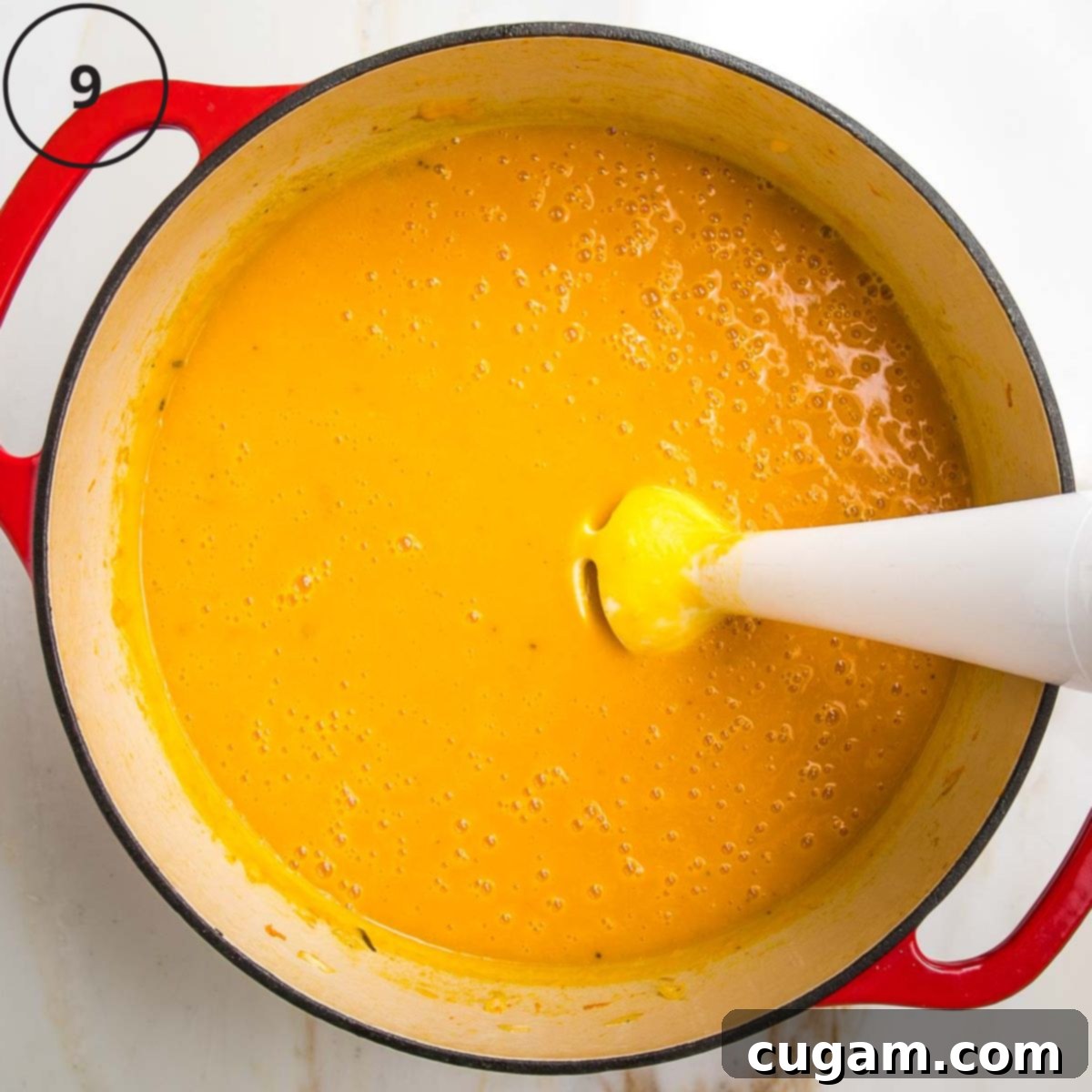 Beautiful orange pureed soup with an immersion blender in a dutch oven.