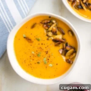 Bright orange creamy soup in a bowl with toasted pepitas, cracked pepper and fresh herbs.