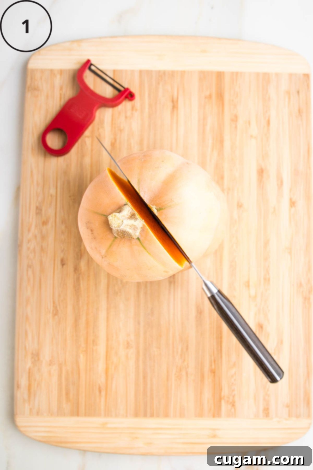 Butternut squash sitting upright on a cutting board. Knife cutting through the stem and down the center.