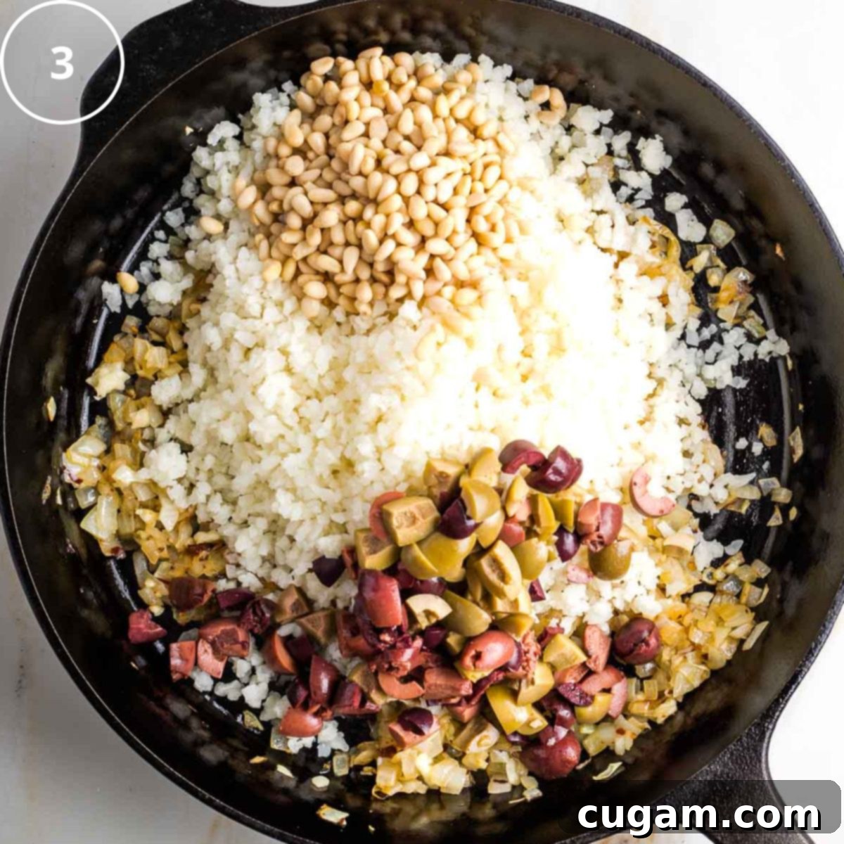 Vibrant Mediterranean Cauliflower Rice 6 Step 3: Cast iron skillet with riced cauliflower, chopped olives and pine nuts over satueed onions.