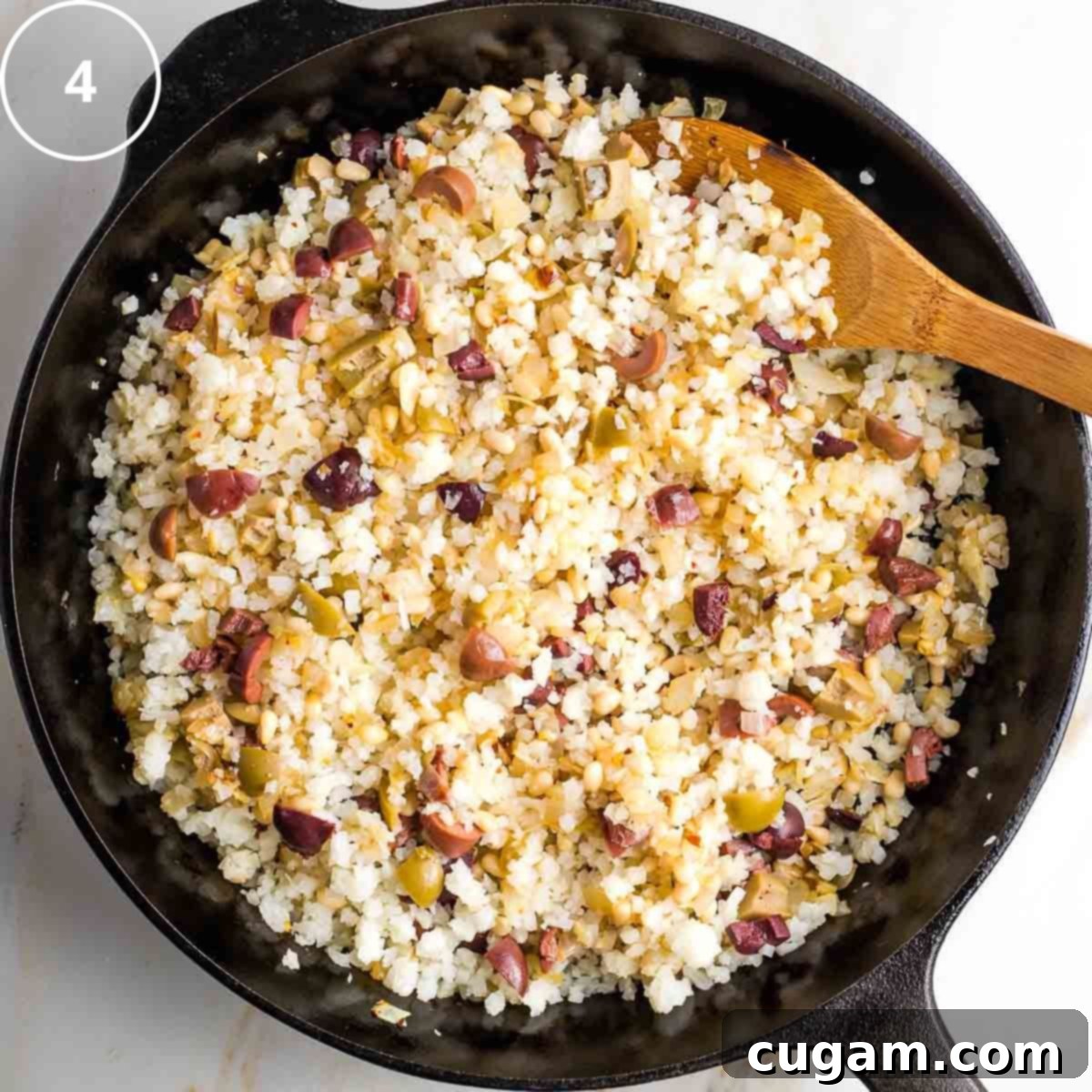 Vibrant Mediterranean Cauliflower Rice 7 Step 4: Mediterranean cauliflower rice with olives and pine nuts in a cast iron pan.