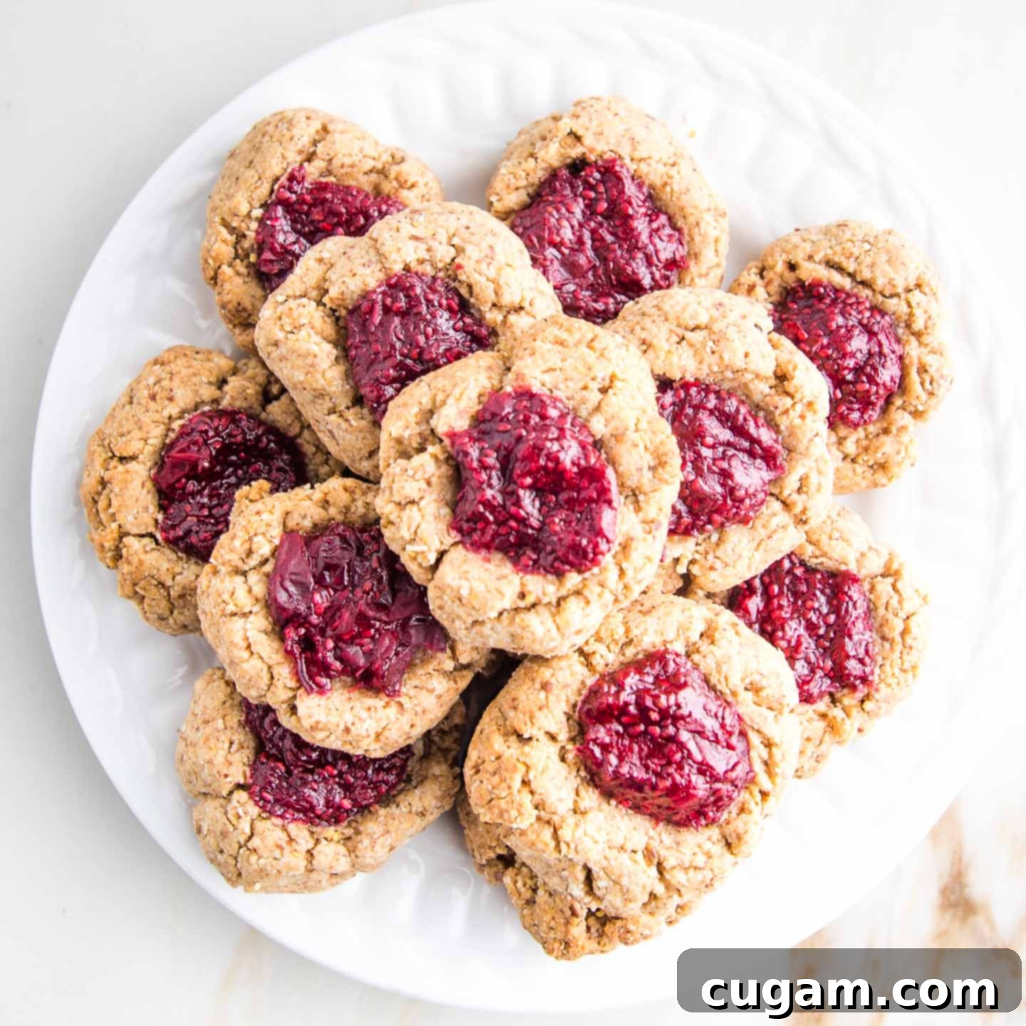 A plate of perfectly baked vegan almond thumbprint cookies filled with bright red jam, ready to be enjoyed.