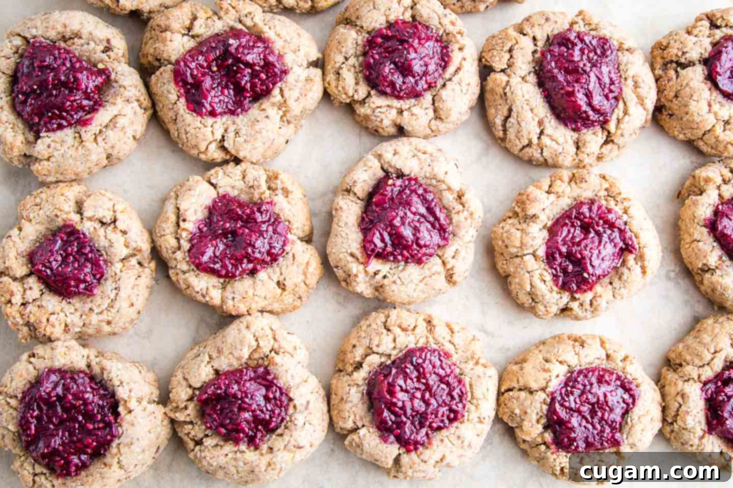 Unbleached parchment paper with thumbprint cookies filled with bright red chia jam, cooling.