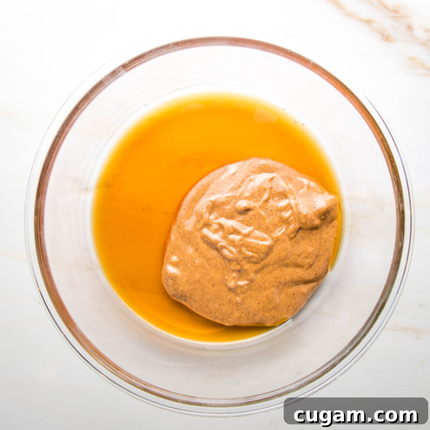 Almond Butter, Maple syrup and almond extract in a large glass bowl, being mixed.