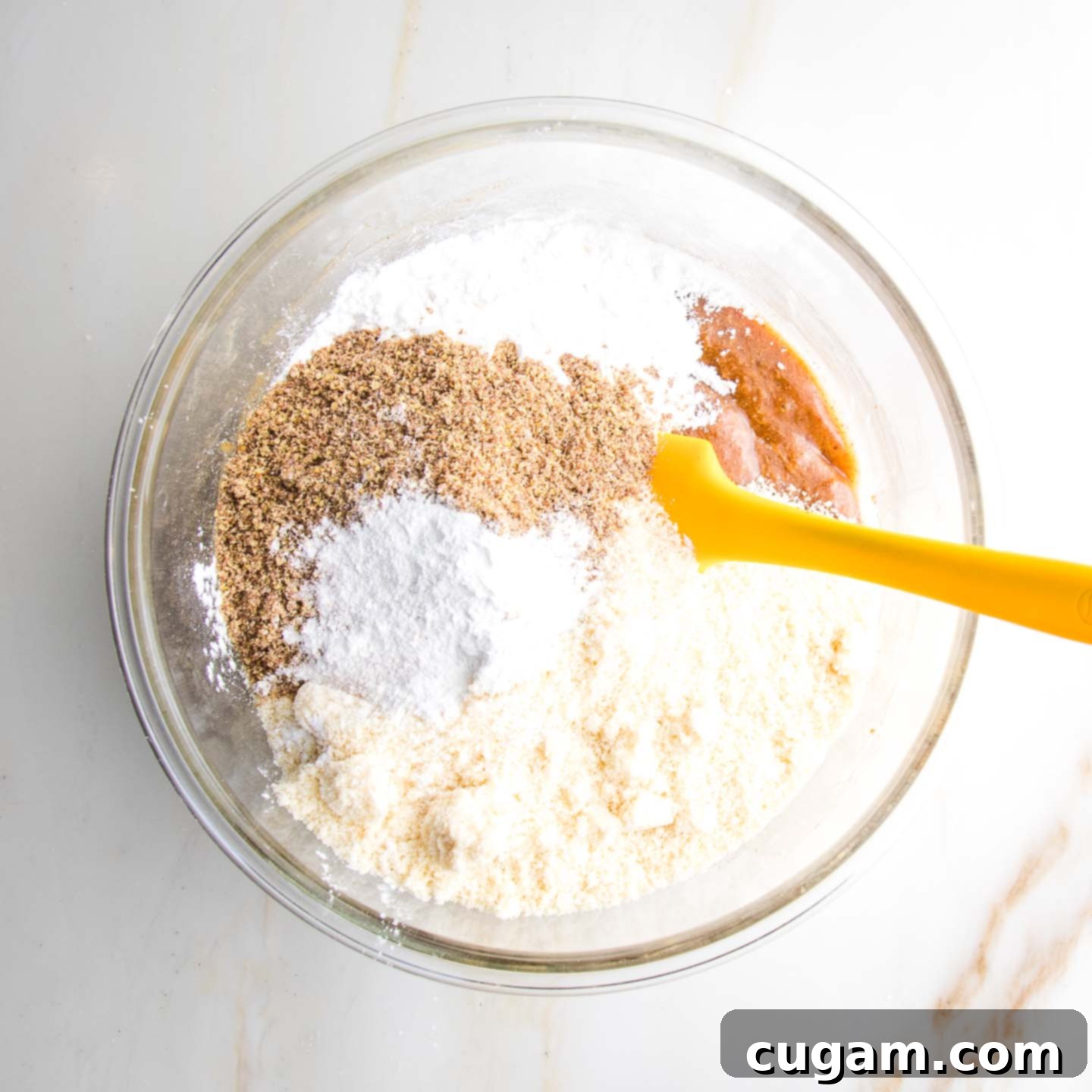 Glass mixing bowl with almond meal, flax meal, arrowroot, baking powder, mixed into maple syrup and almond butter for thumbprint cookies.
