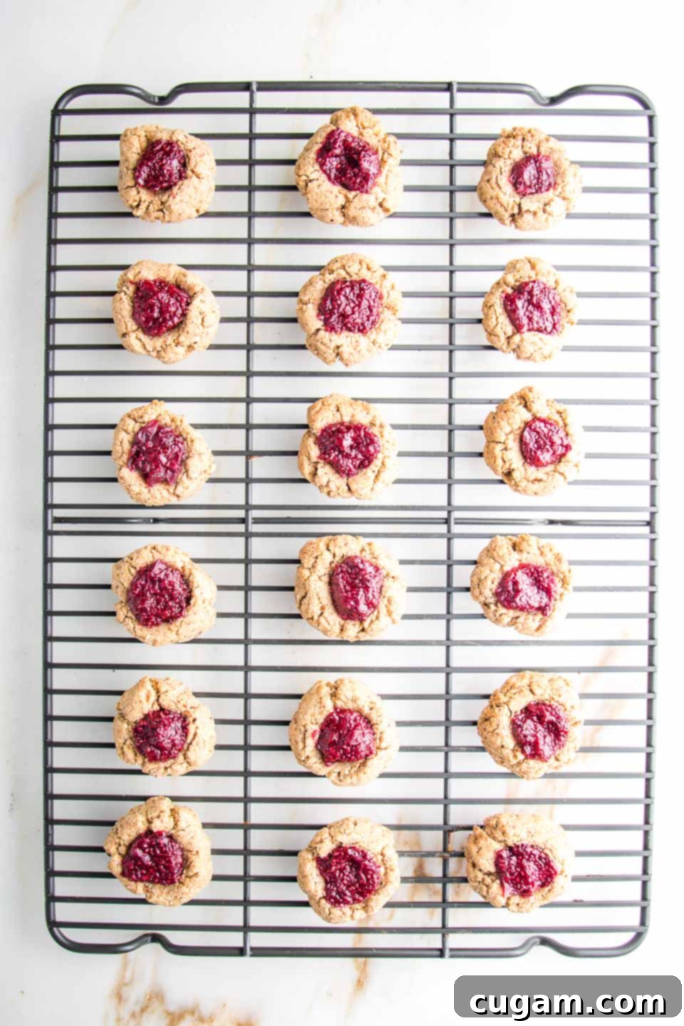 Wire rack with thumbprint cookies filled with bright red jam cooling completely.