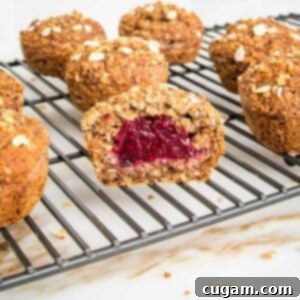 Healthy Jam Filled Oatmeal Muffins cooling on a wire rack. One muffin is cut open to show the delicious jam inside.