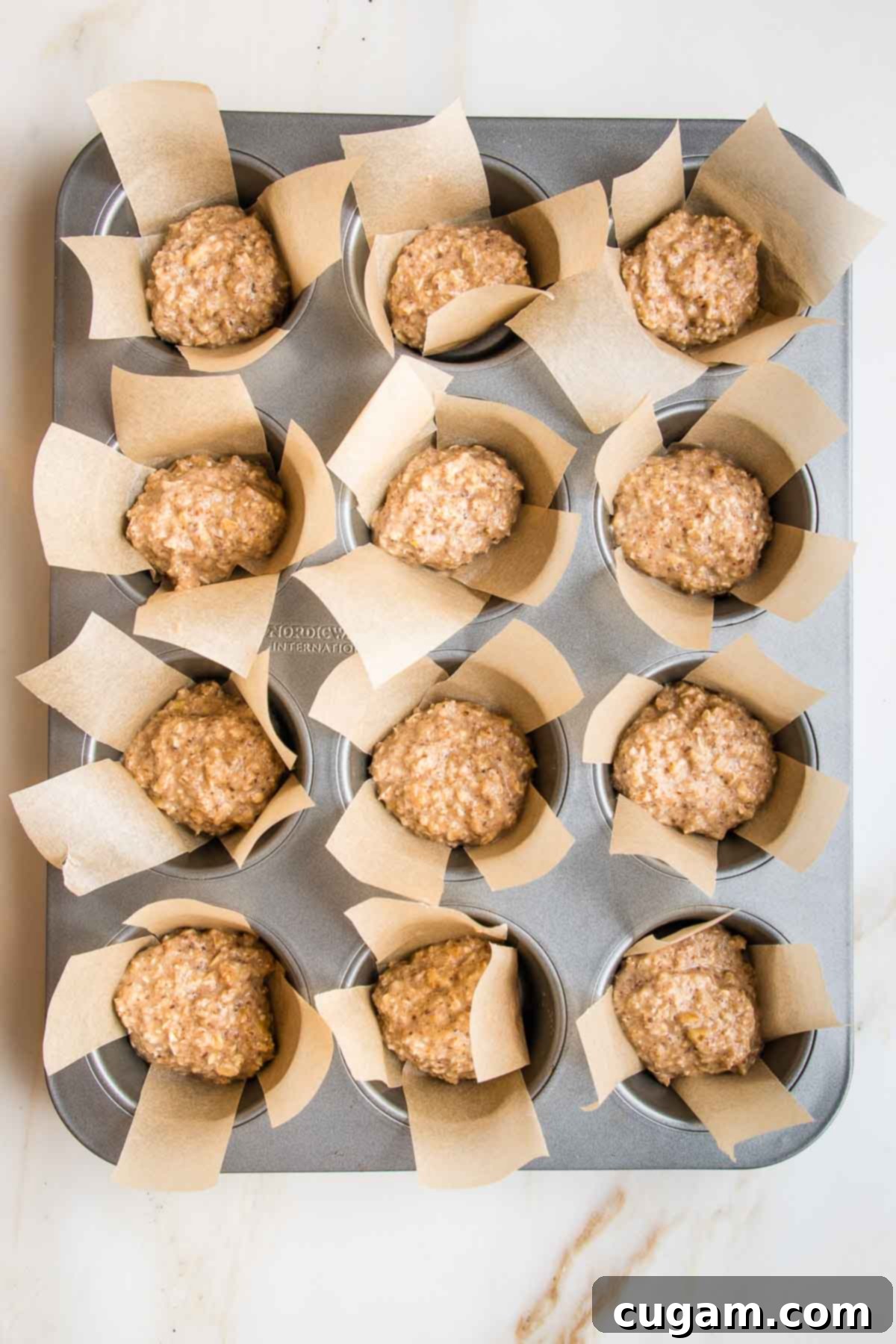 A muffin tin, perfectly lined with individual strips of parchment paper, with each cup about halfway filled with the wholesome oatmeal batter.