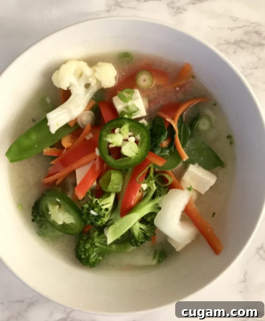 A close-up of a bowl of simple miso soup with colorful vegetables and tofu.