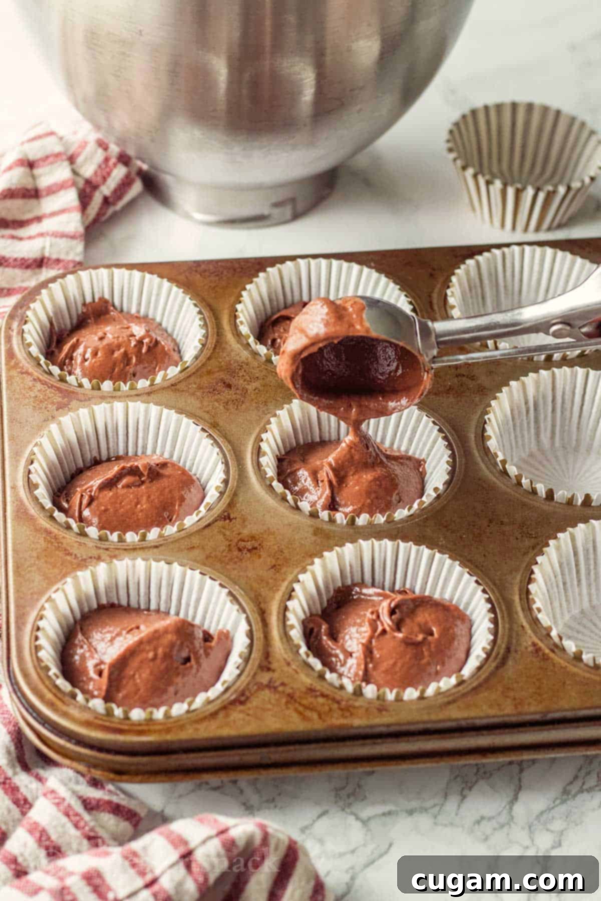 Decadent Chocolate Caramel Cupcakes 6 Metal scoop pouring chocolate cake batter into cupcake liners in a metal baking pan.