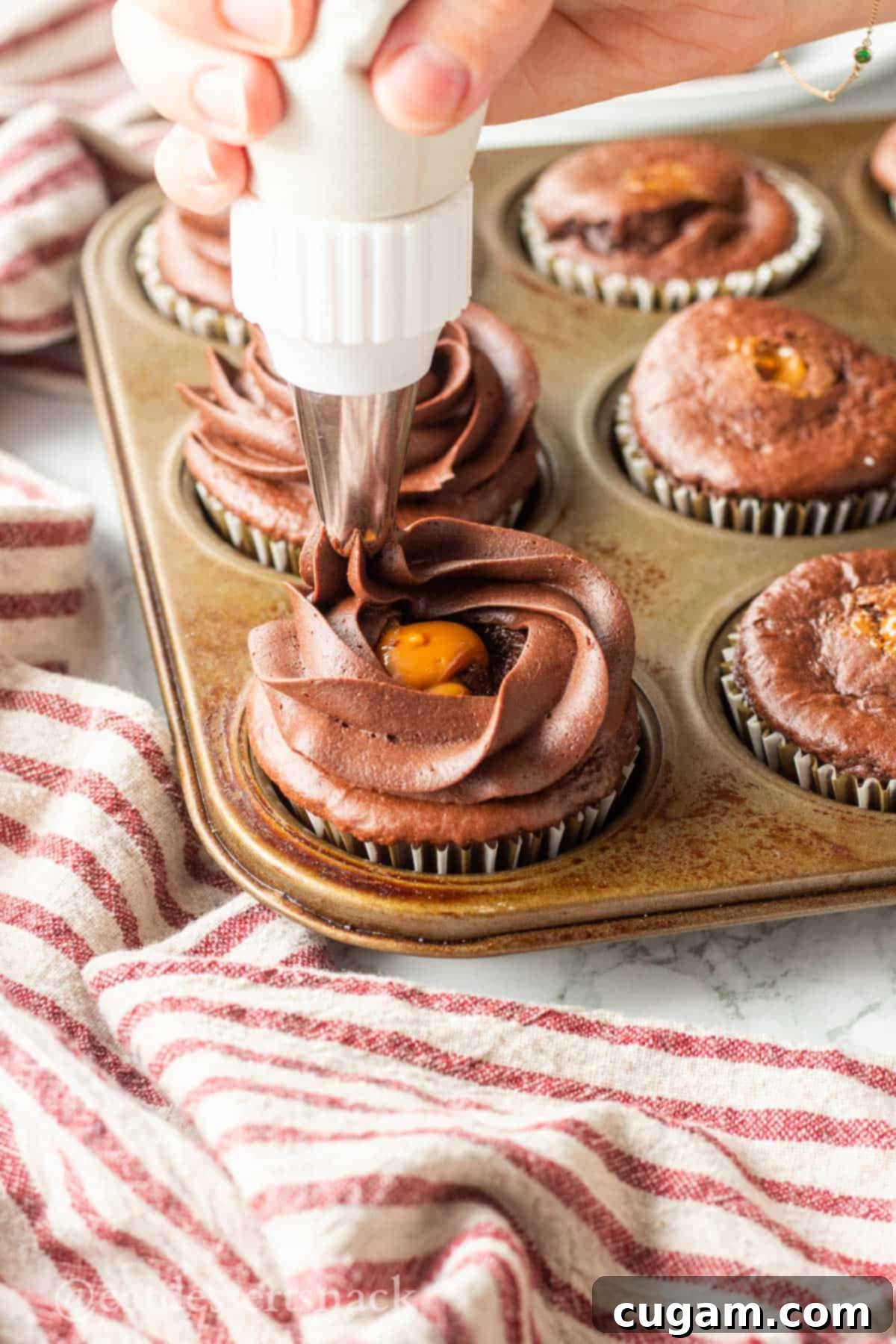 Decadent Chocolate Caramel Cupcakes 9 Hand piping chocolate frosting onto caramel filled chocolate cupcakes.