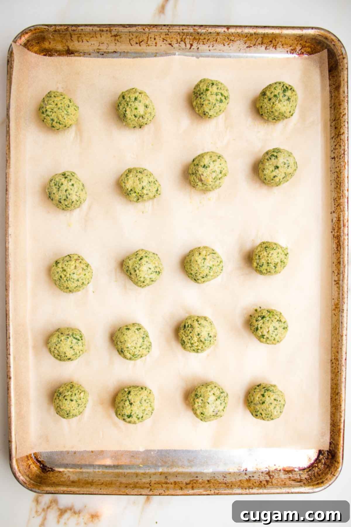 Falafel balls spaced out on a parchment lined baking tray. 