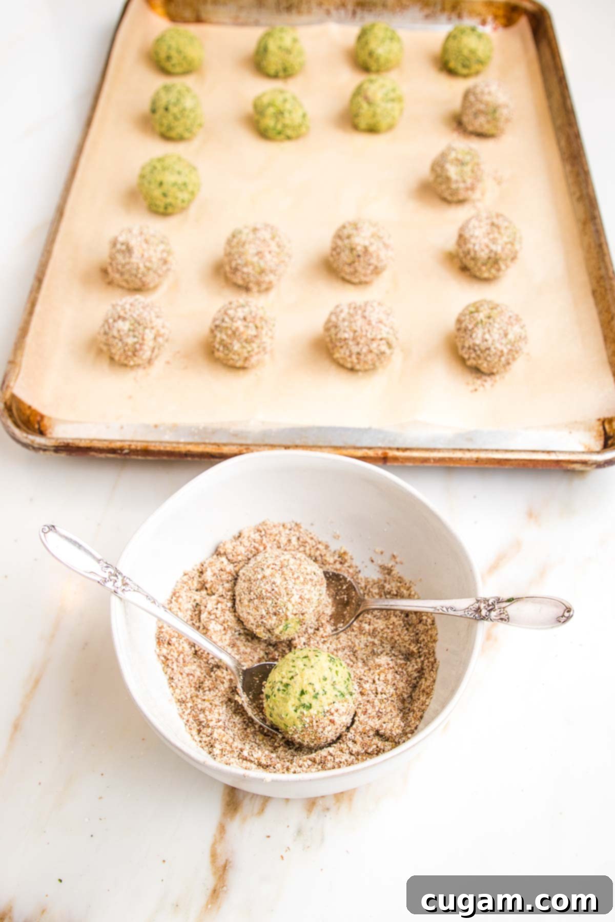 Falafel balls lined up on a baking tray. A bowl to coat balls in flax/almond meal mixture before baking.