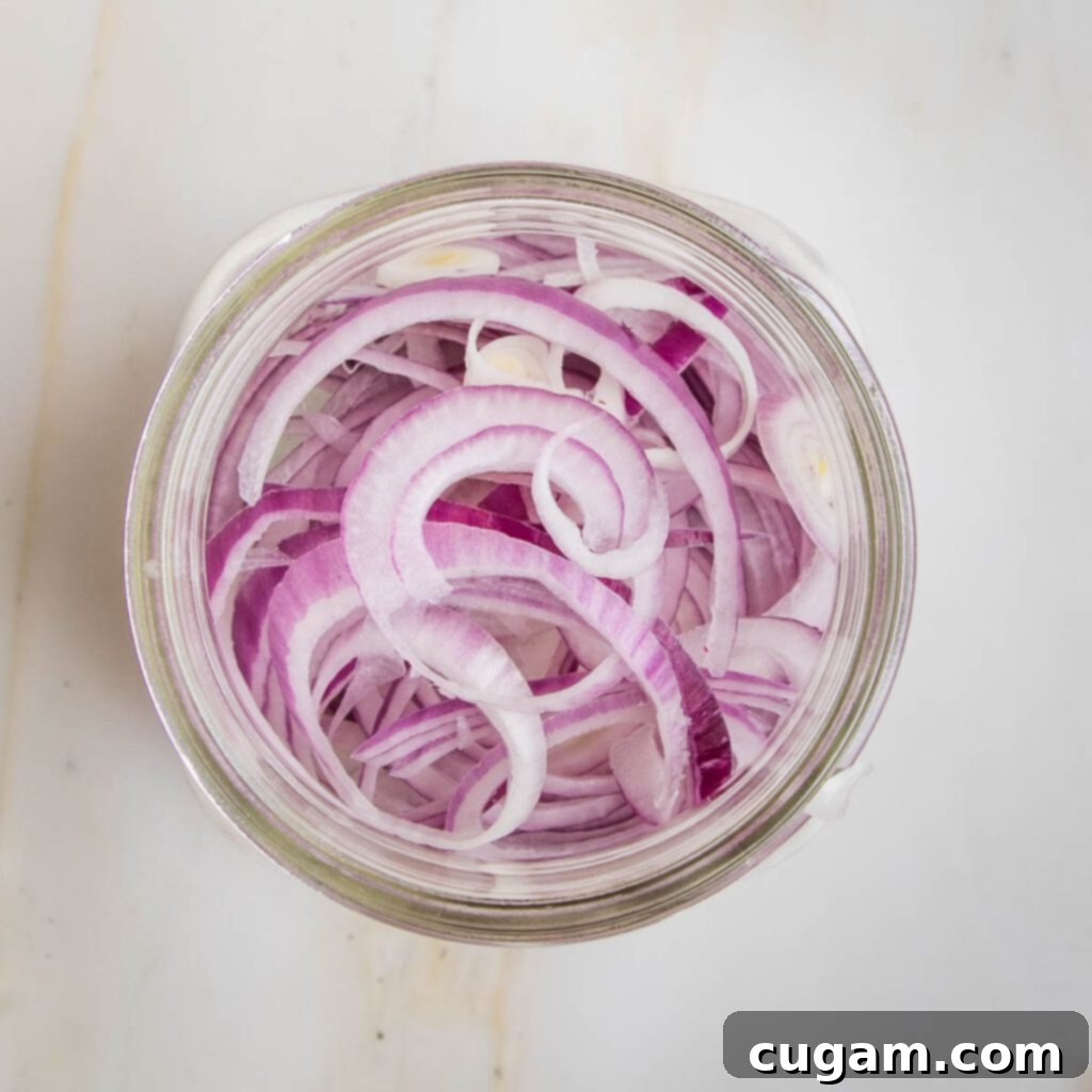 Vinegar mixture being poured over red onions in a jar.
