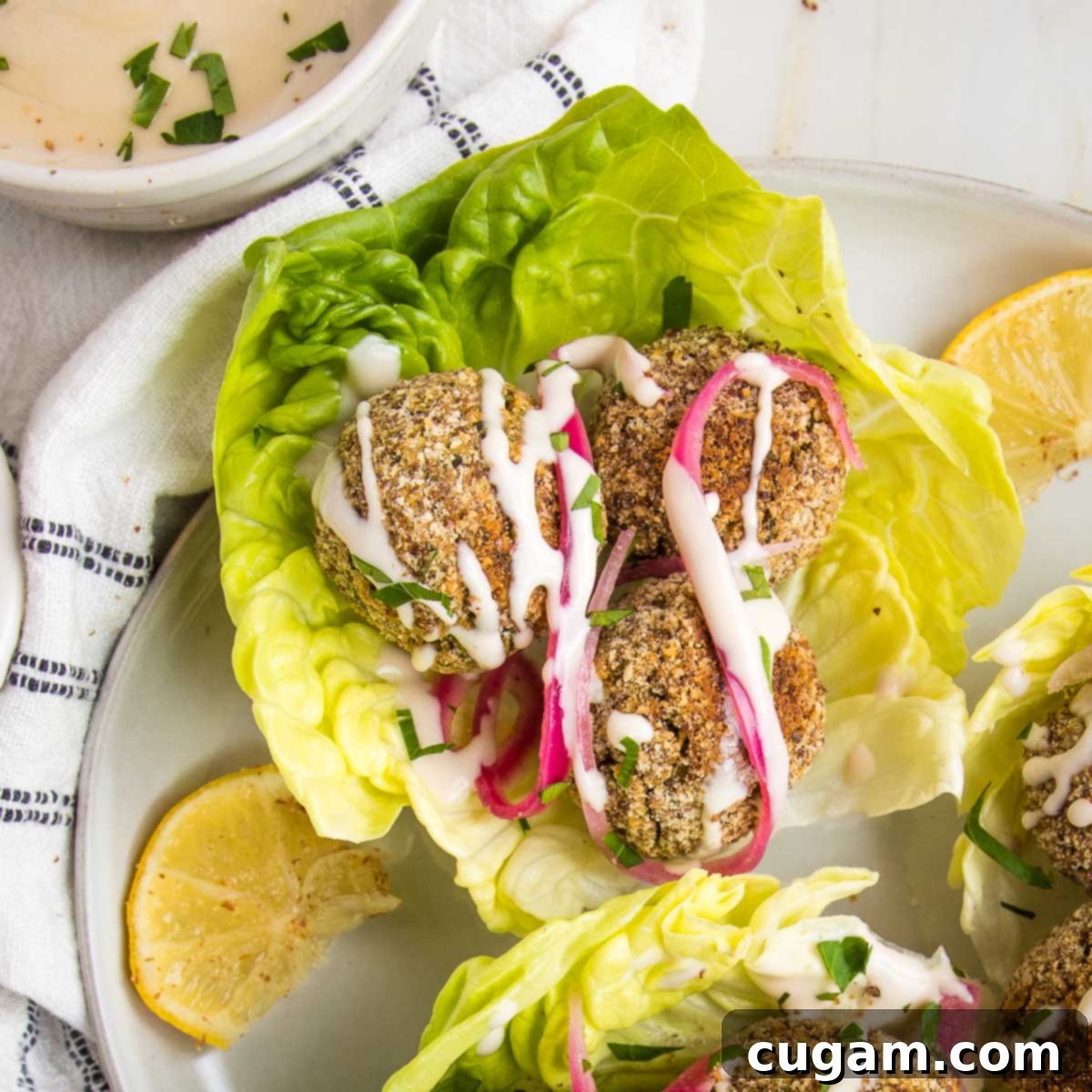 Falafel balls on a lettuce leaf with tahini drizzle and pickled onions.
