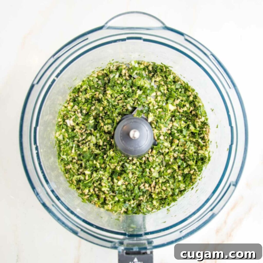 Food processor bowl with ground herbs, nuts, onions and garlic.