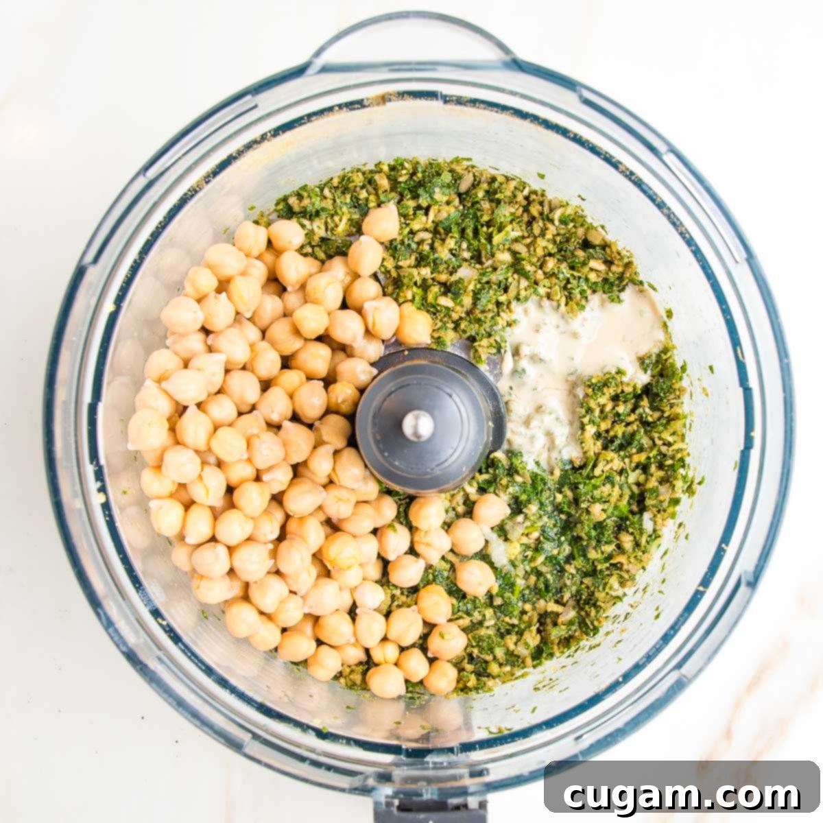 Ground fresh herbs, spices and seeds in the bowl of a food processor with chickpeas and tahini.