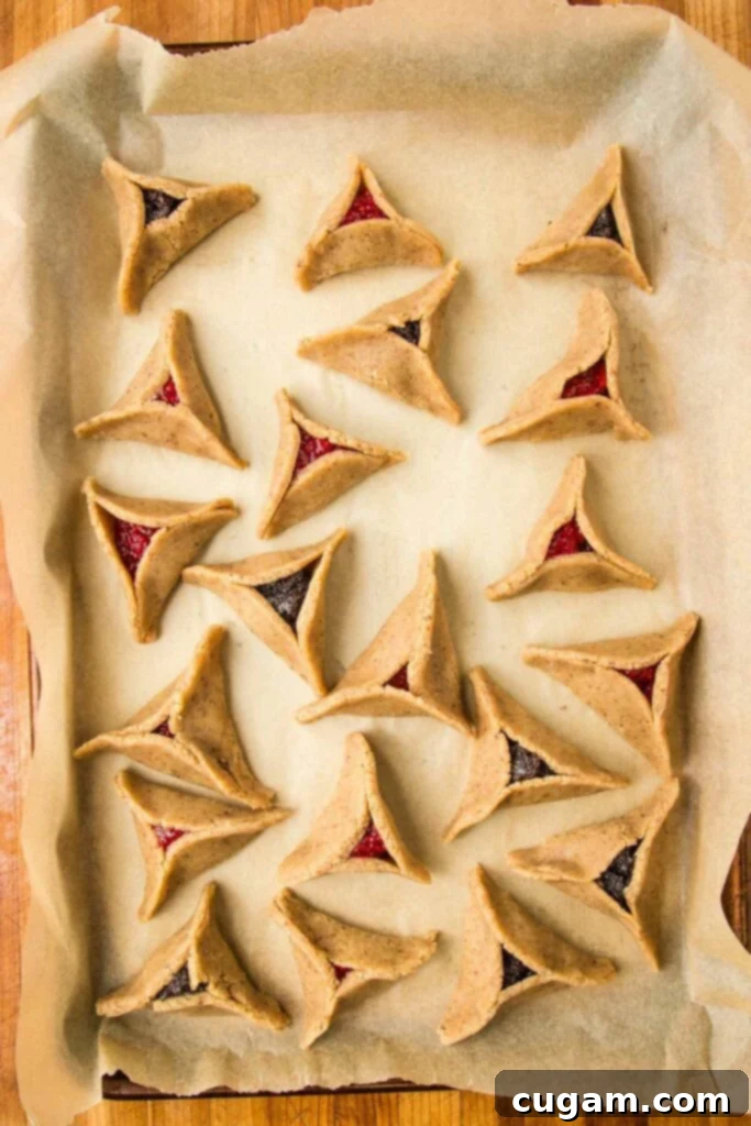 Cookie tray, lined with parchment paper, filled with baked hamentashcen filled with poppy seed or raspberry jam.