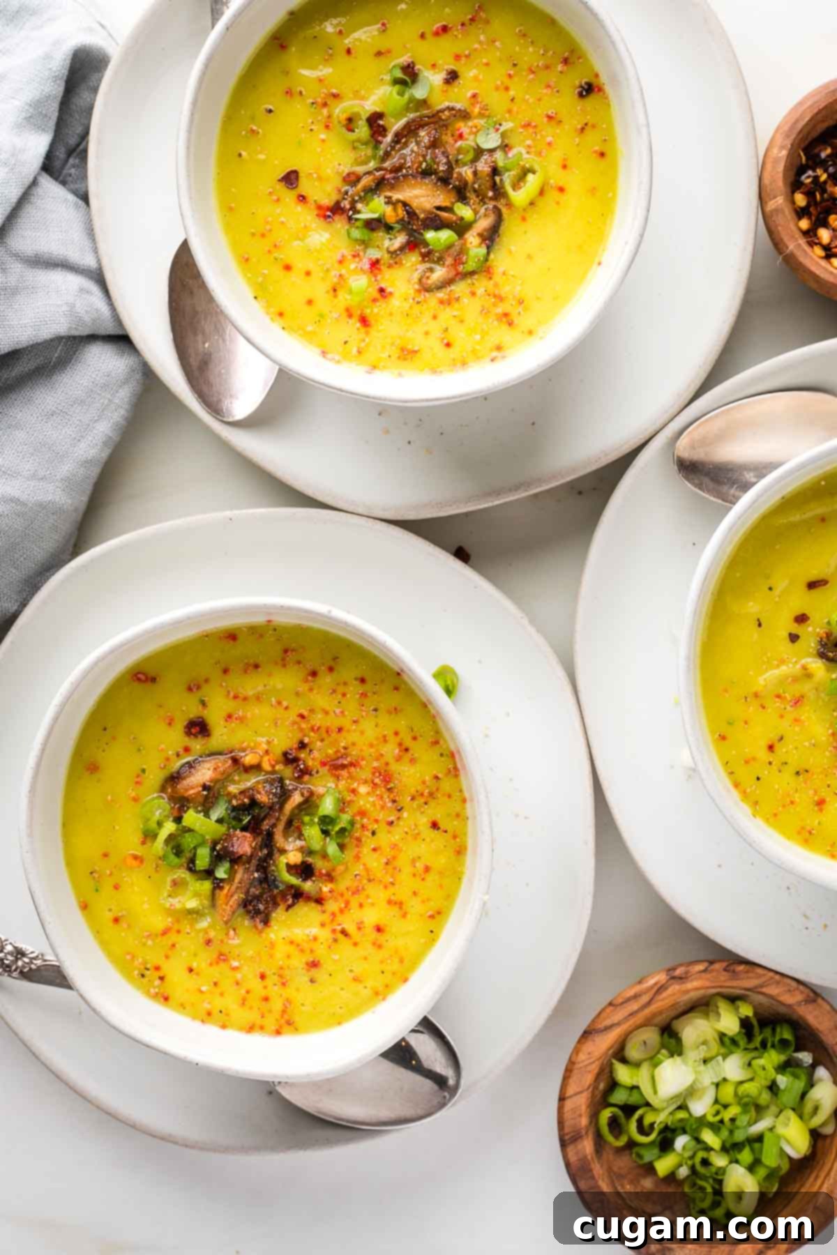 Creamy yellow pureed vegetable soup with sauteed mushrooms, scallions and crushed red pepper on the surface. 