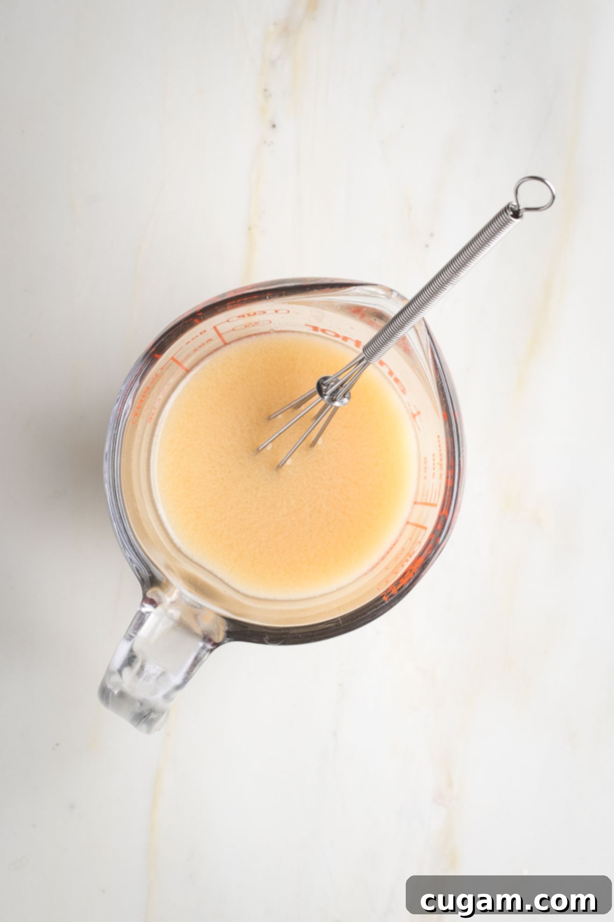 Glass pyrex cup with a whisk and cloudy beige liquid.