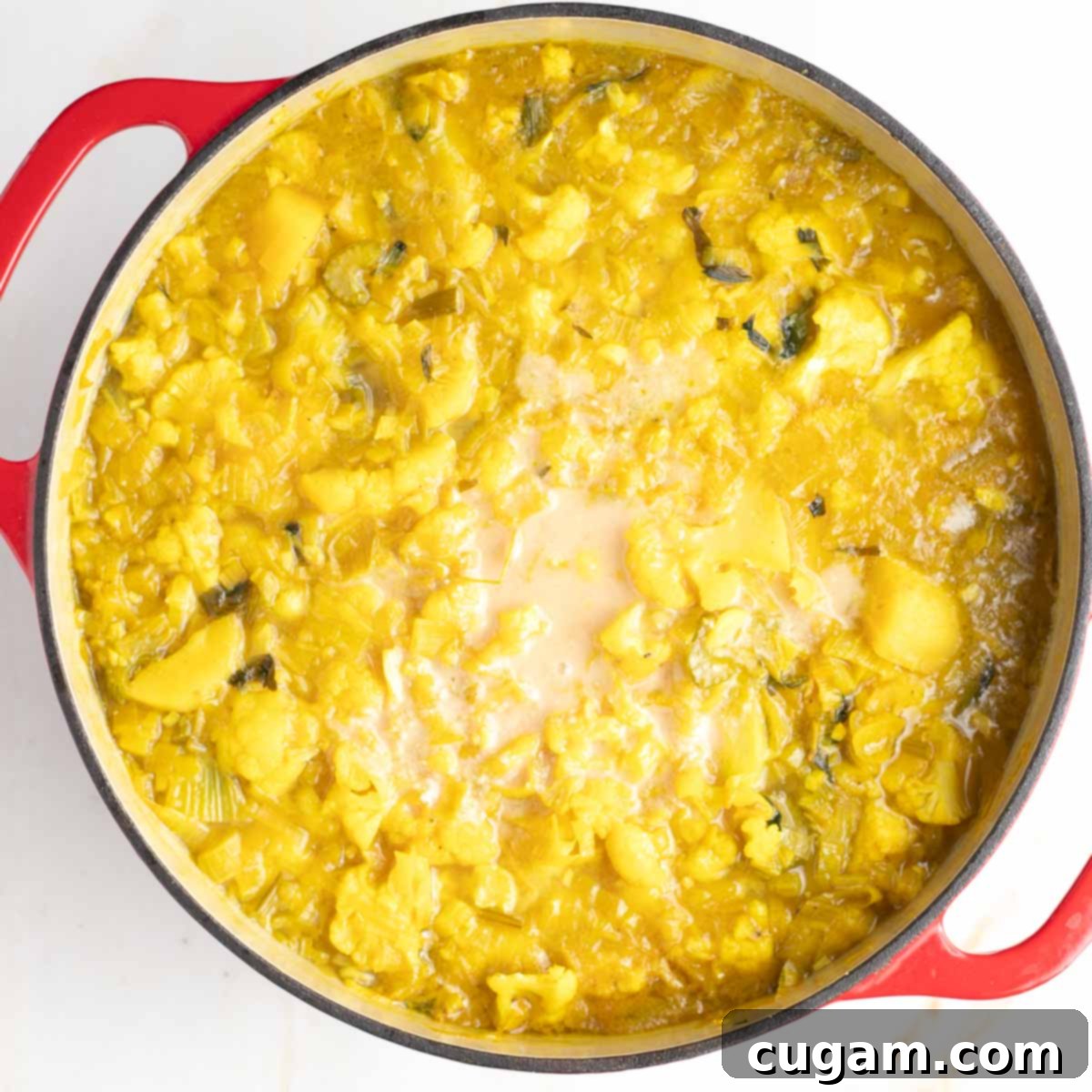 Dutch oven with yellow chunky vegetable soup, and a cloud of beige liquid in the center.