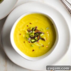 Bowl of creamy yellow soup with sauteed mushrooms, scallions and red pepper floating on top.