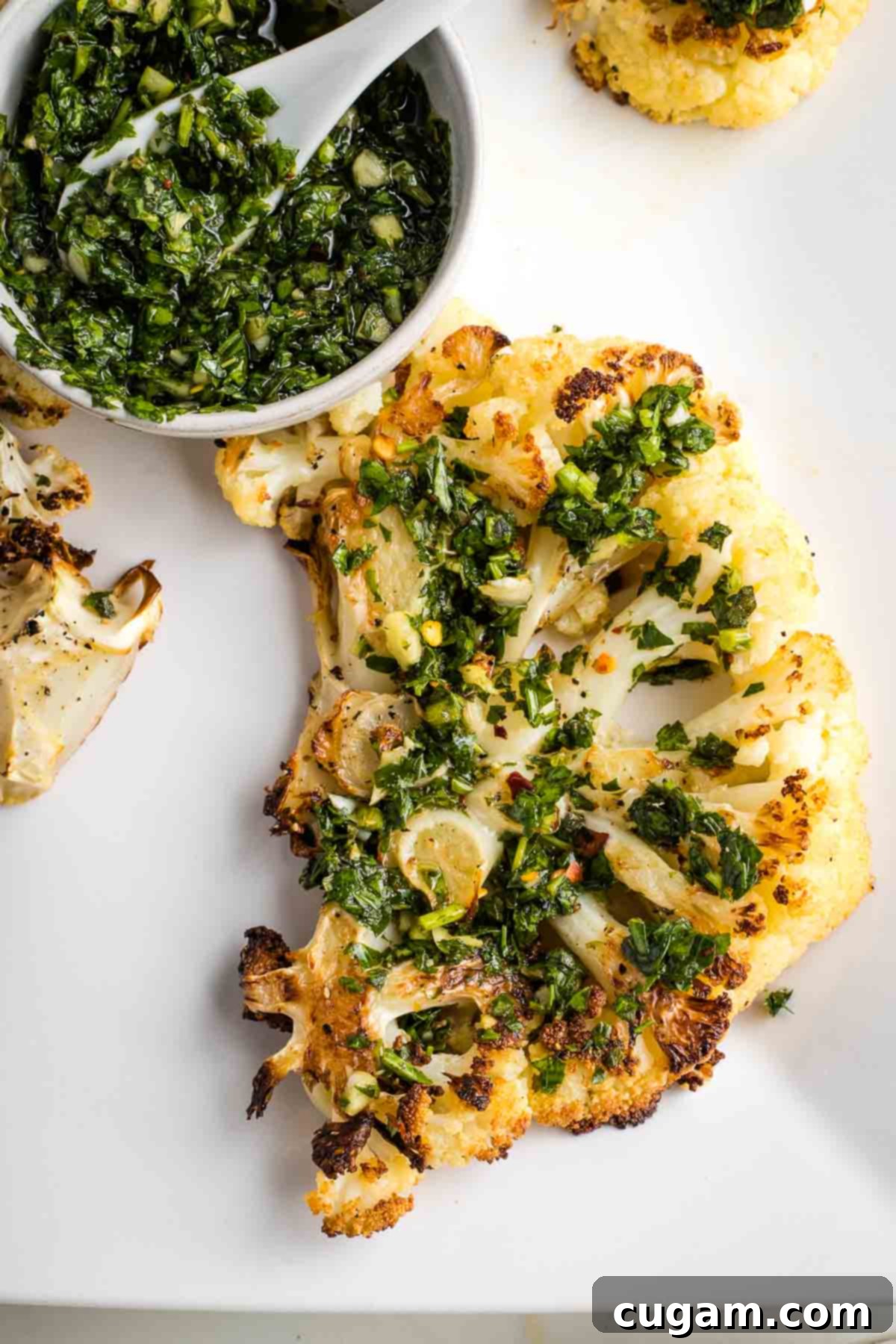 A single, perfectly cooked cauliflower steak adorned with chimichurri, with a small bowl of extra sauce for personal preference.