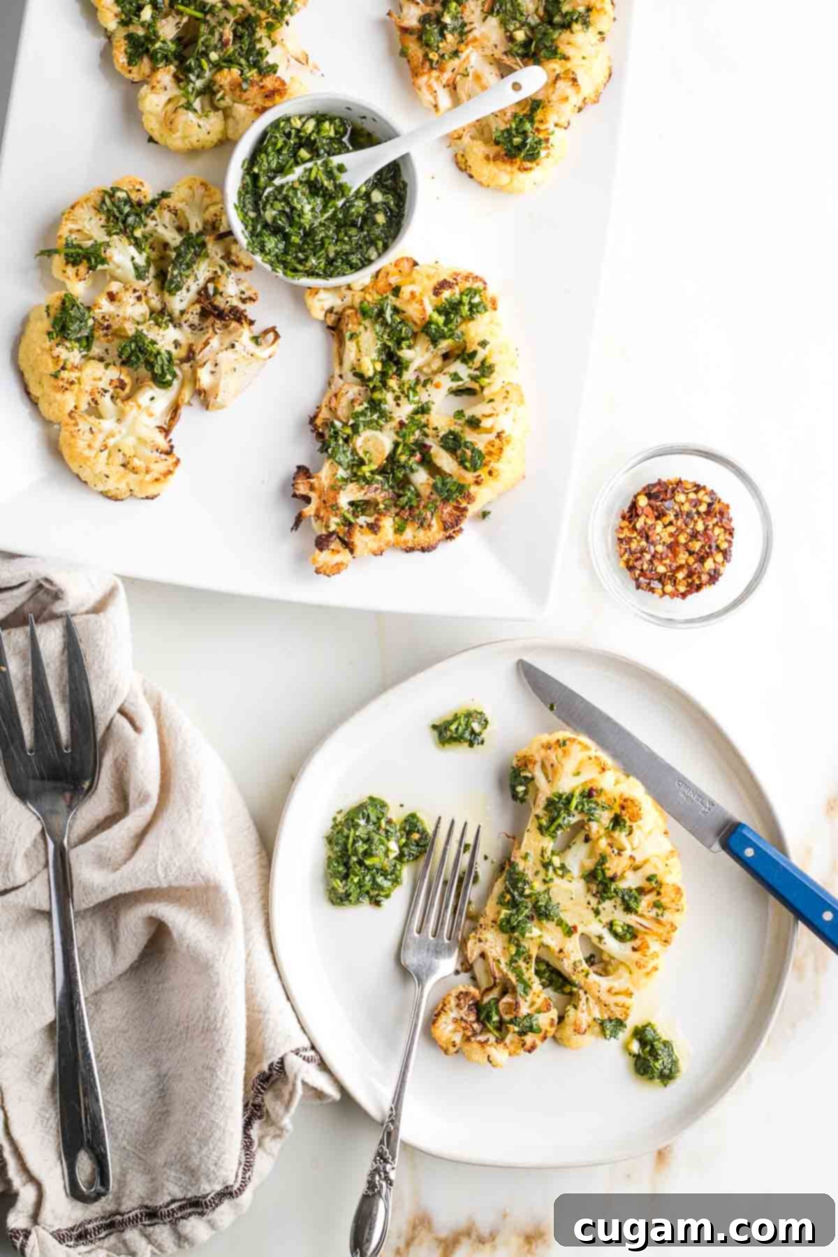 A beautiful platter of golden-brown cauliflower steaks, a generous bowl of chimichurri, and a single steak on a plate with a steak knife, ready to be enjoyed.