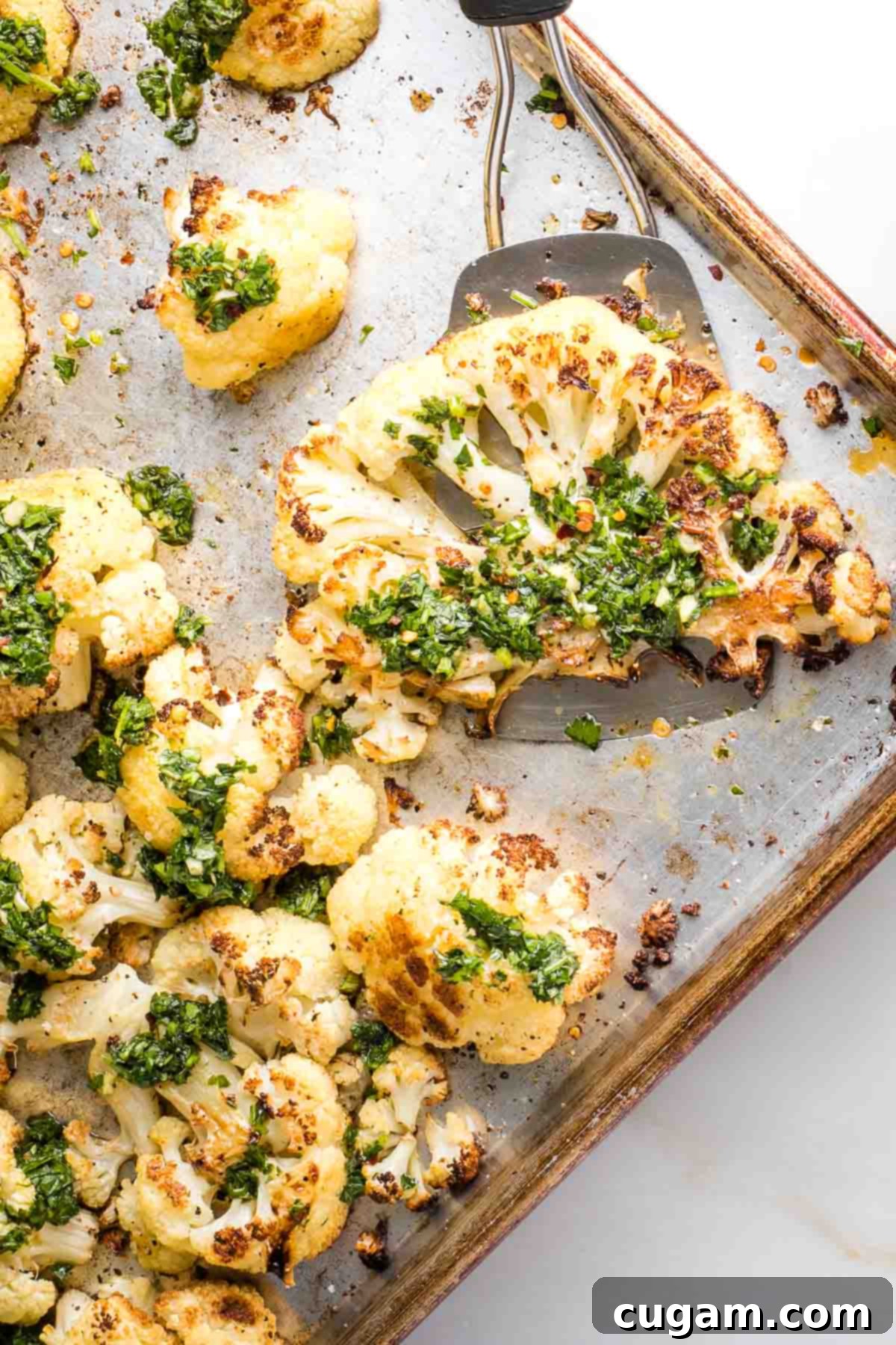 Spatula serving a golden-brown cauliflower steak with a generous dollop of green chimichurri sauce off a sheet pan, ready to be enjoyed.