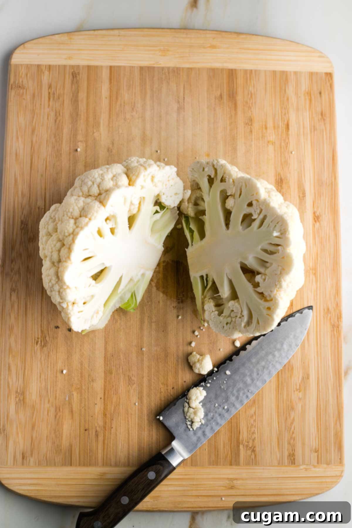 Head of cauliflower positioned flat on a wooden board, cleanly cut through the center into two halves.