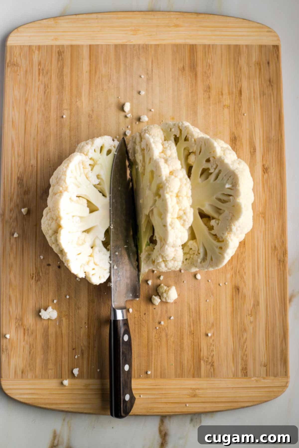 A half-head of cauliflower sliced into thick, uniform steaks on a wooden cutting board.