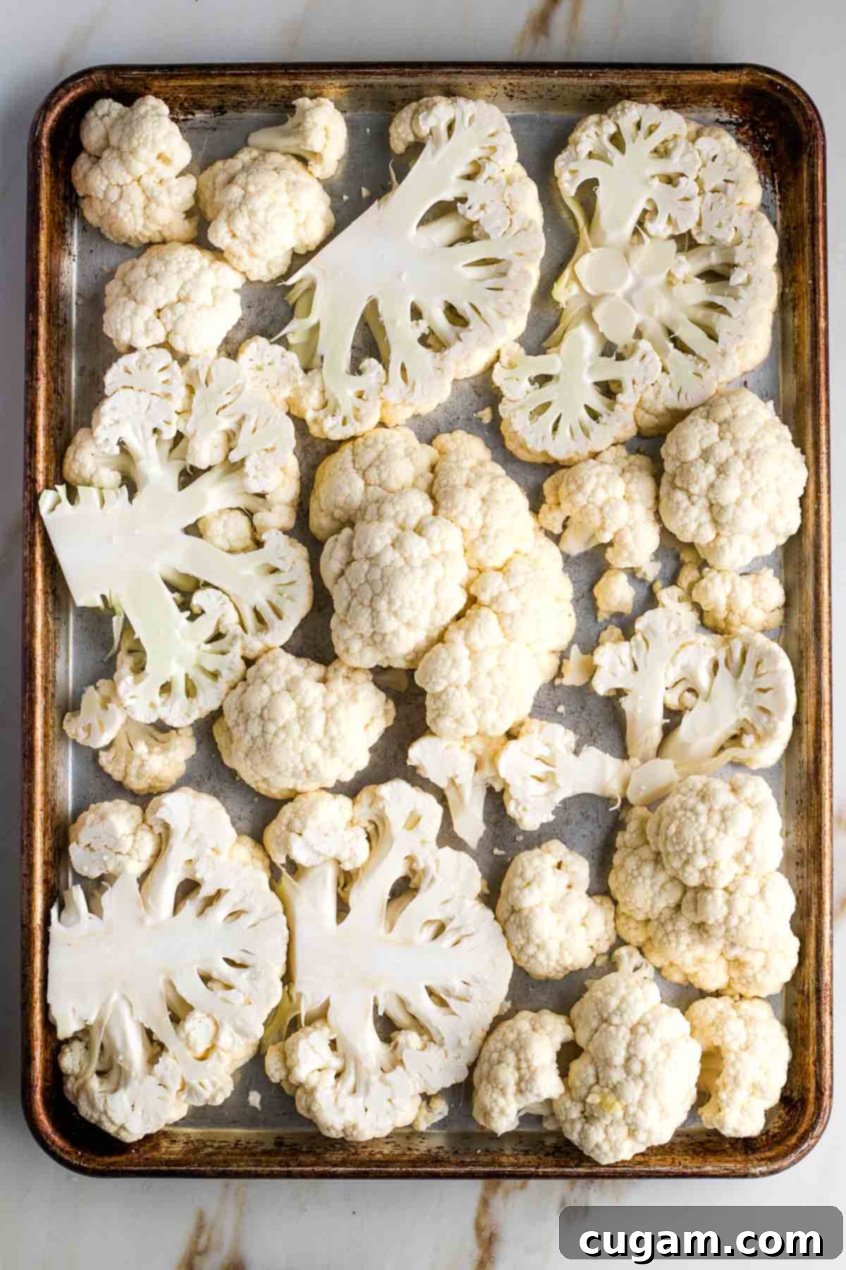 Large rimmed baking sheet with evenly spaced cauliflower steaks and florets arranged in a single layer, ready for roasting.
