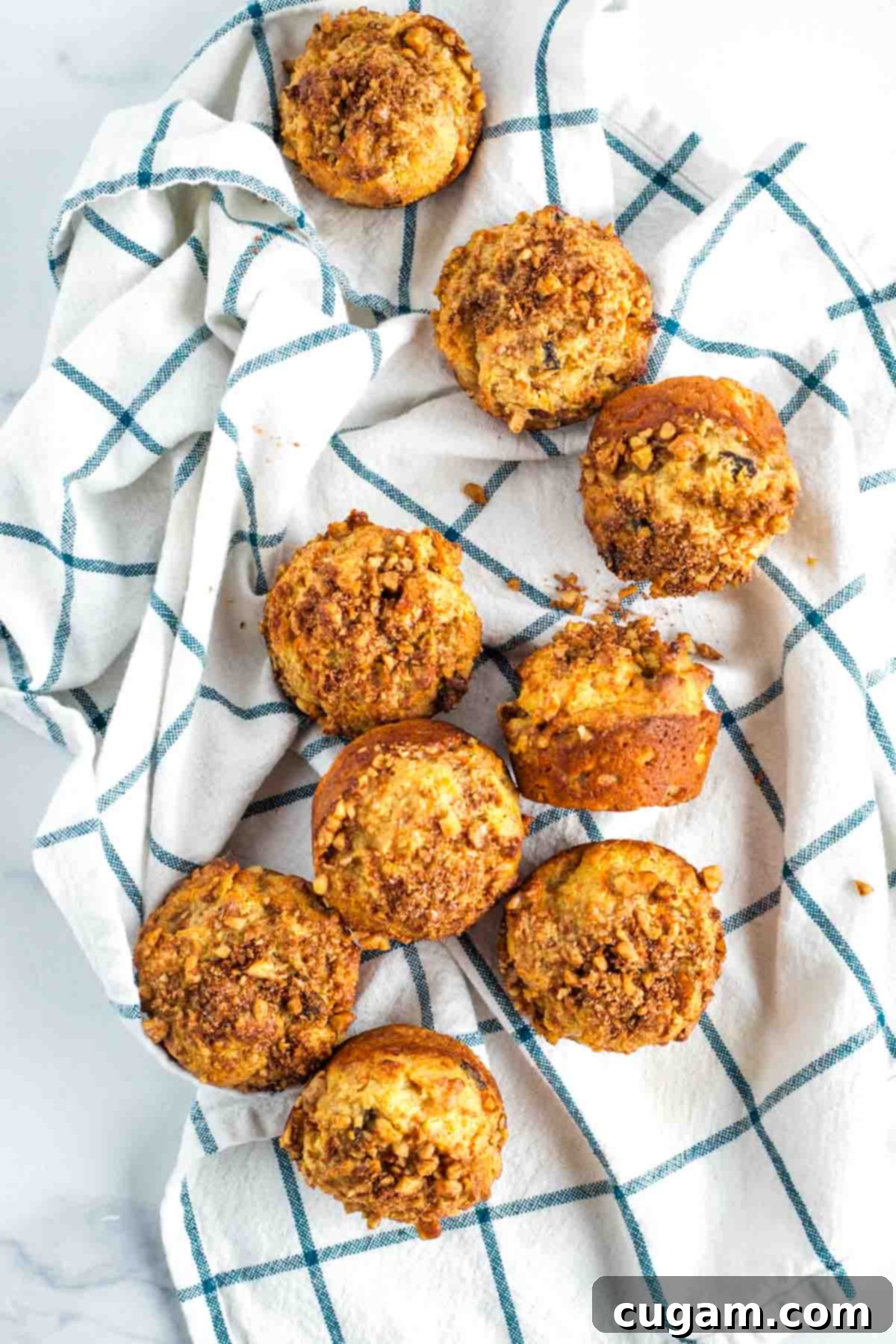 Carrot cake muffins strewn out on a white tea towel with navy loose grid pattern. Delicious gluten-free and grain-free muffins made with almond flour, perfect for breakfast or a healthy snack.