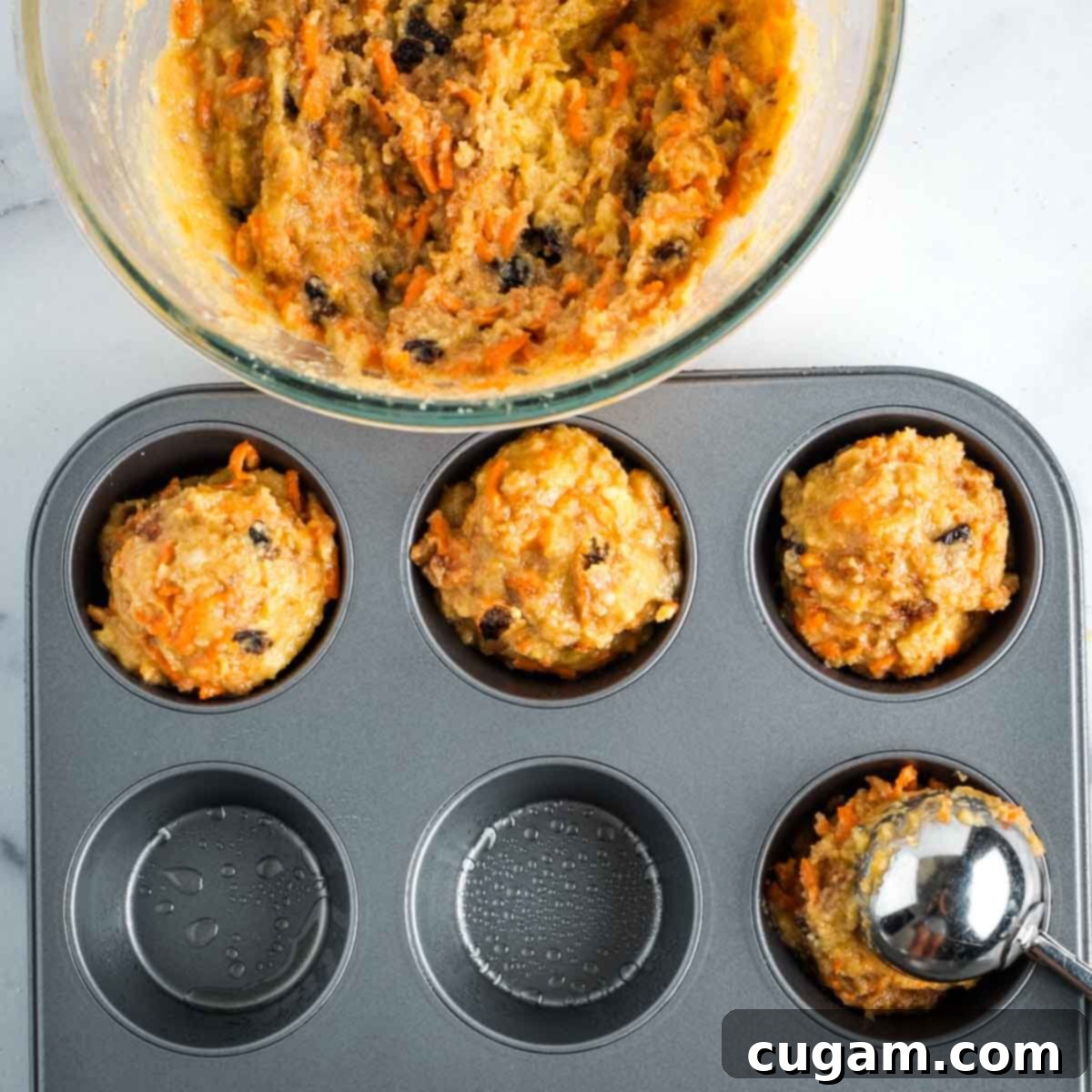 Filling muffin tins generously with carrot muffin batter.